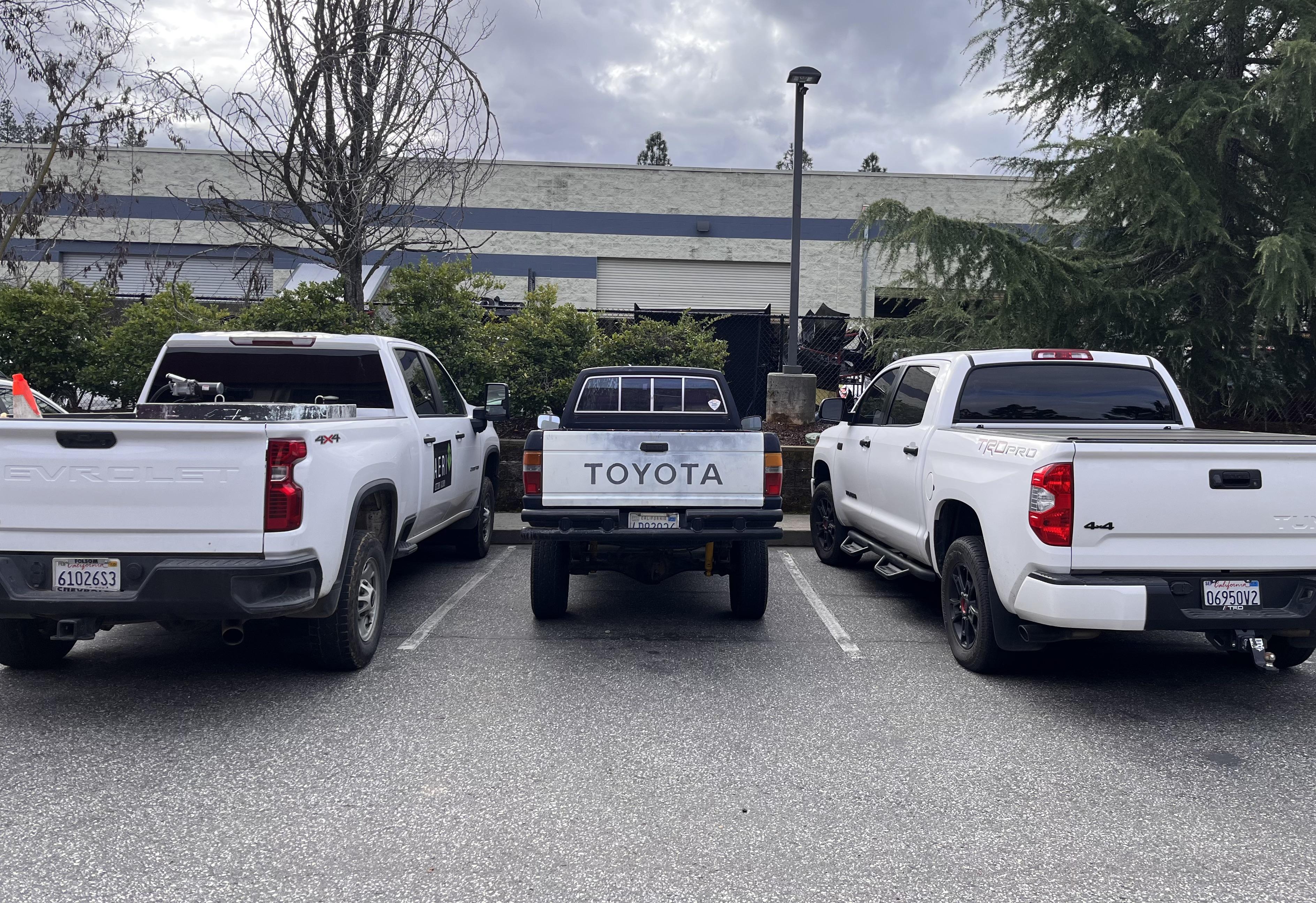 Three pickup trucks parked in a row in a parking lot. The center truck has a visible "Toyota" label on its back