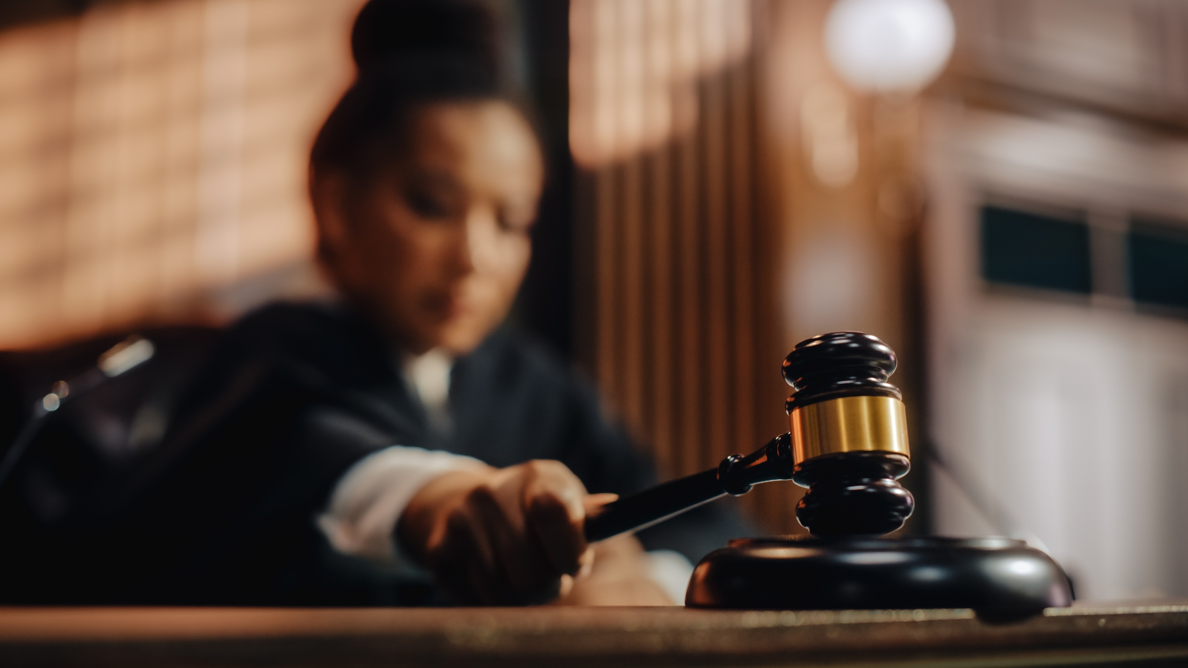 A judge in a courtroom strikes a gavel on a desk, focusing on a legal decision