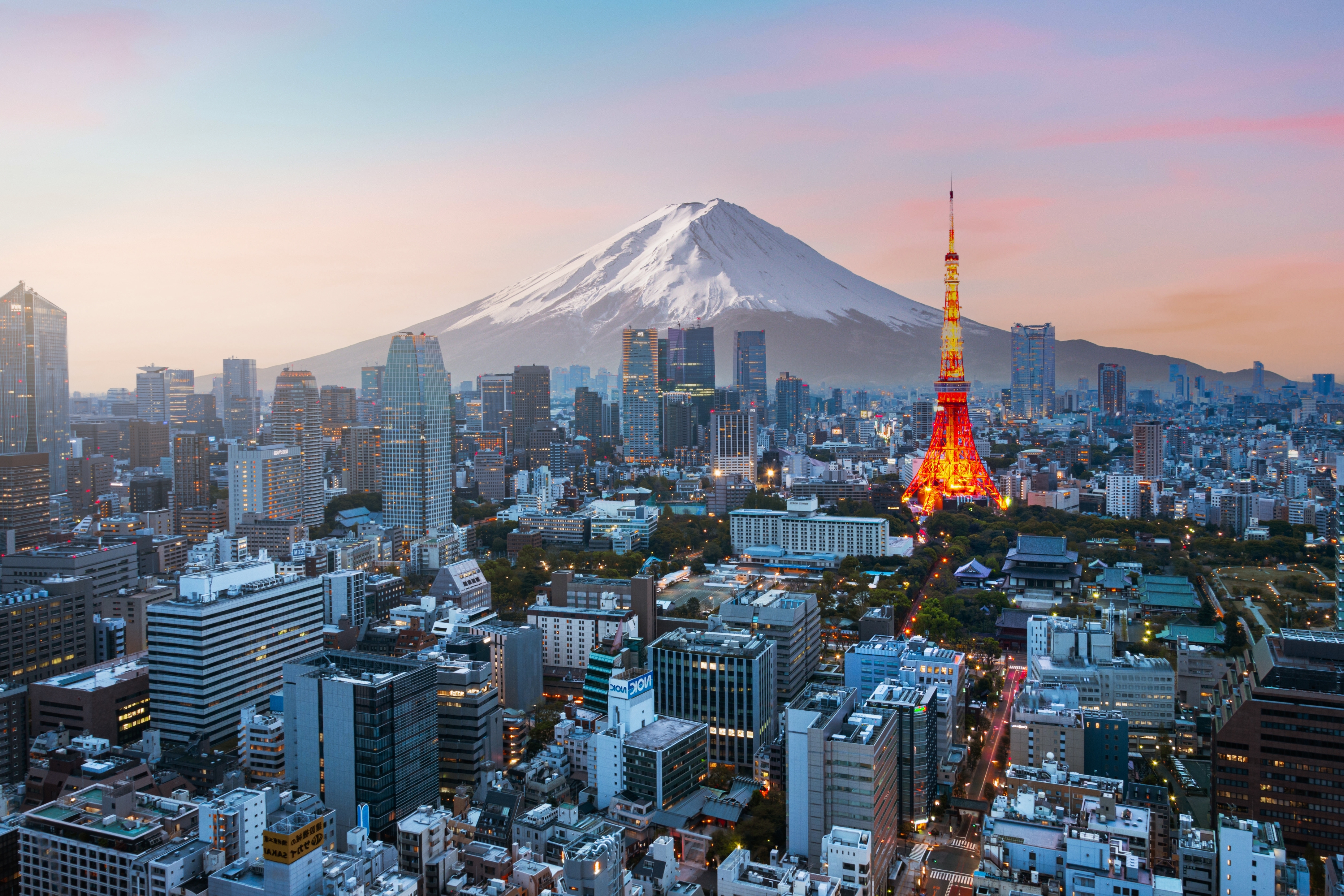 City skyline with Mount Fuji in the background and a lit-up tower in the foreground, during sunset