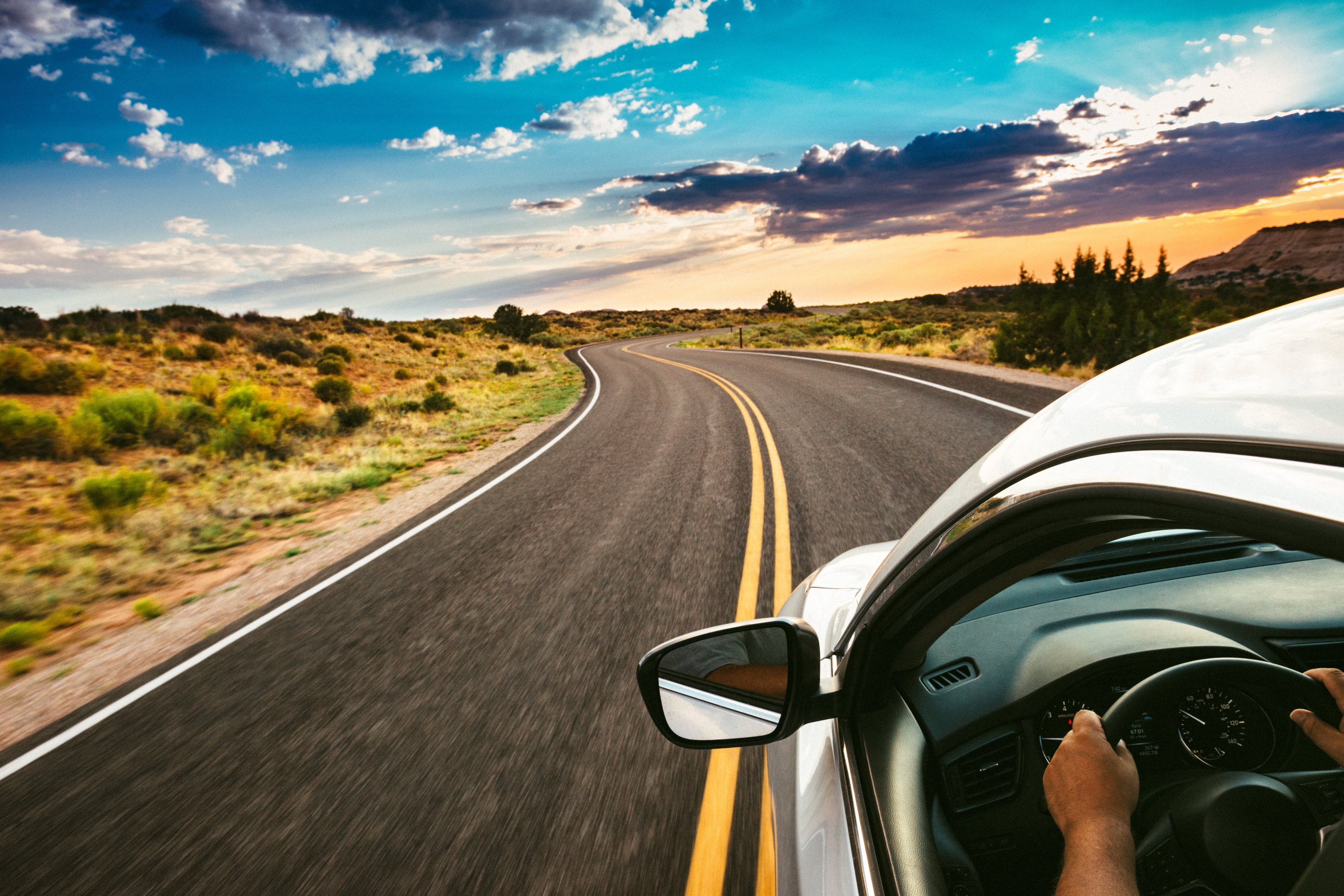 Driver's perspective of a car on a winding road through a scenic landscape under a partly cloudy sky