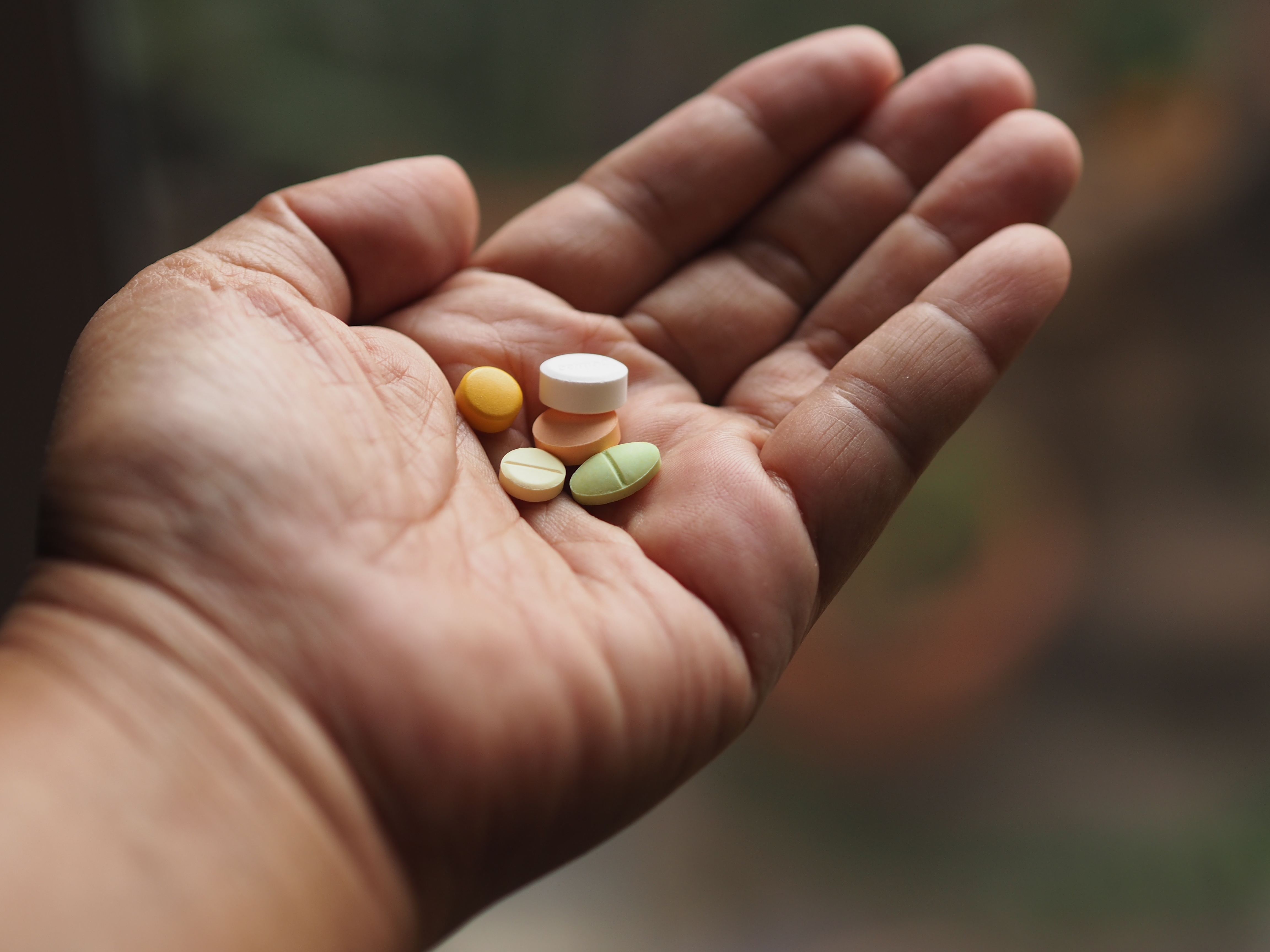 An open hand holding various pills, showcasing different shapes and sizes