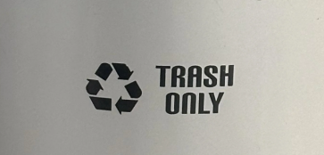Silver trash can labeled "Trash Only" with a recycling symbol, next to a wheelchair