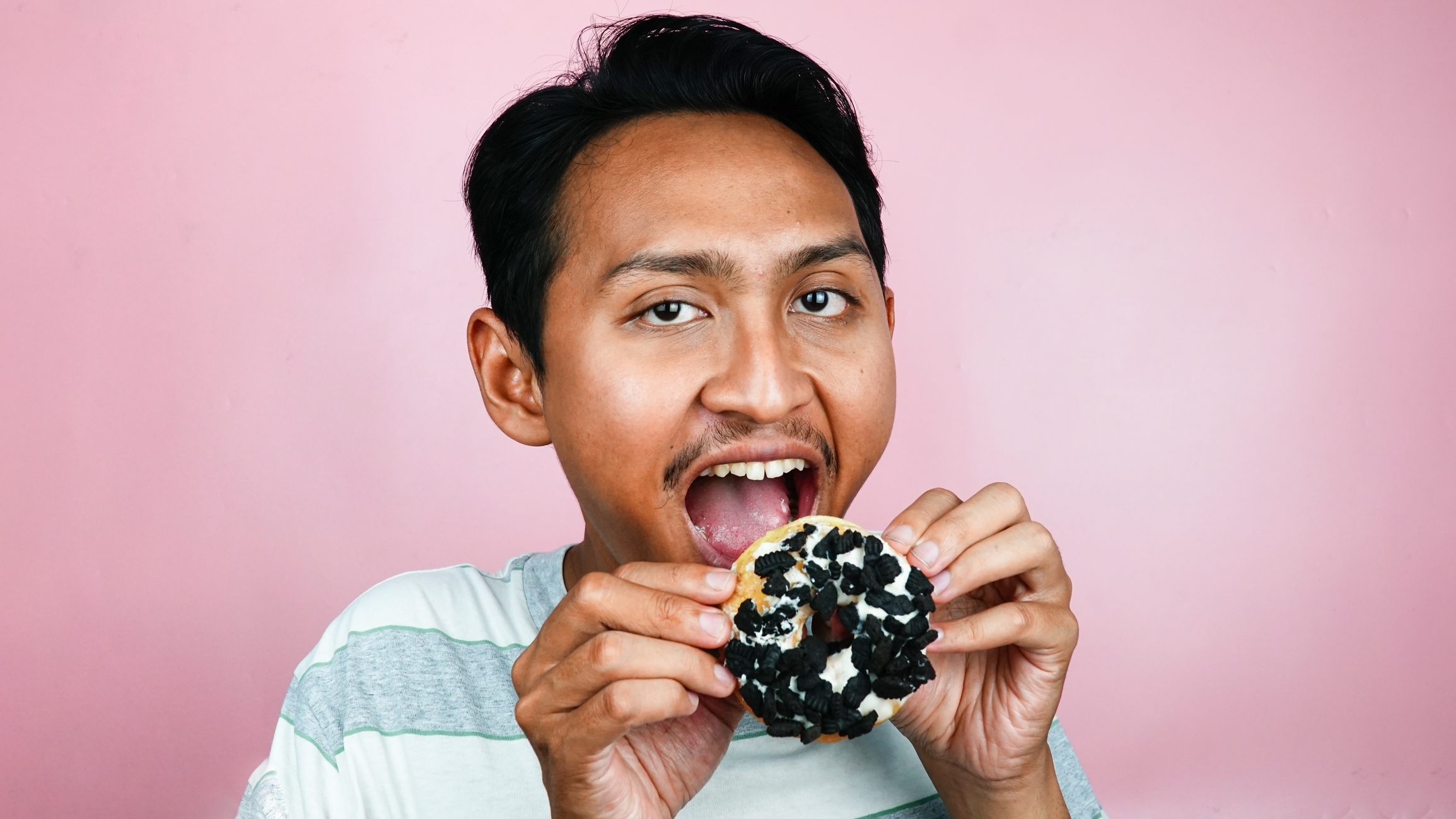 Person smiling while holding and about to eat a cookie topped with chocolate pieces