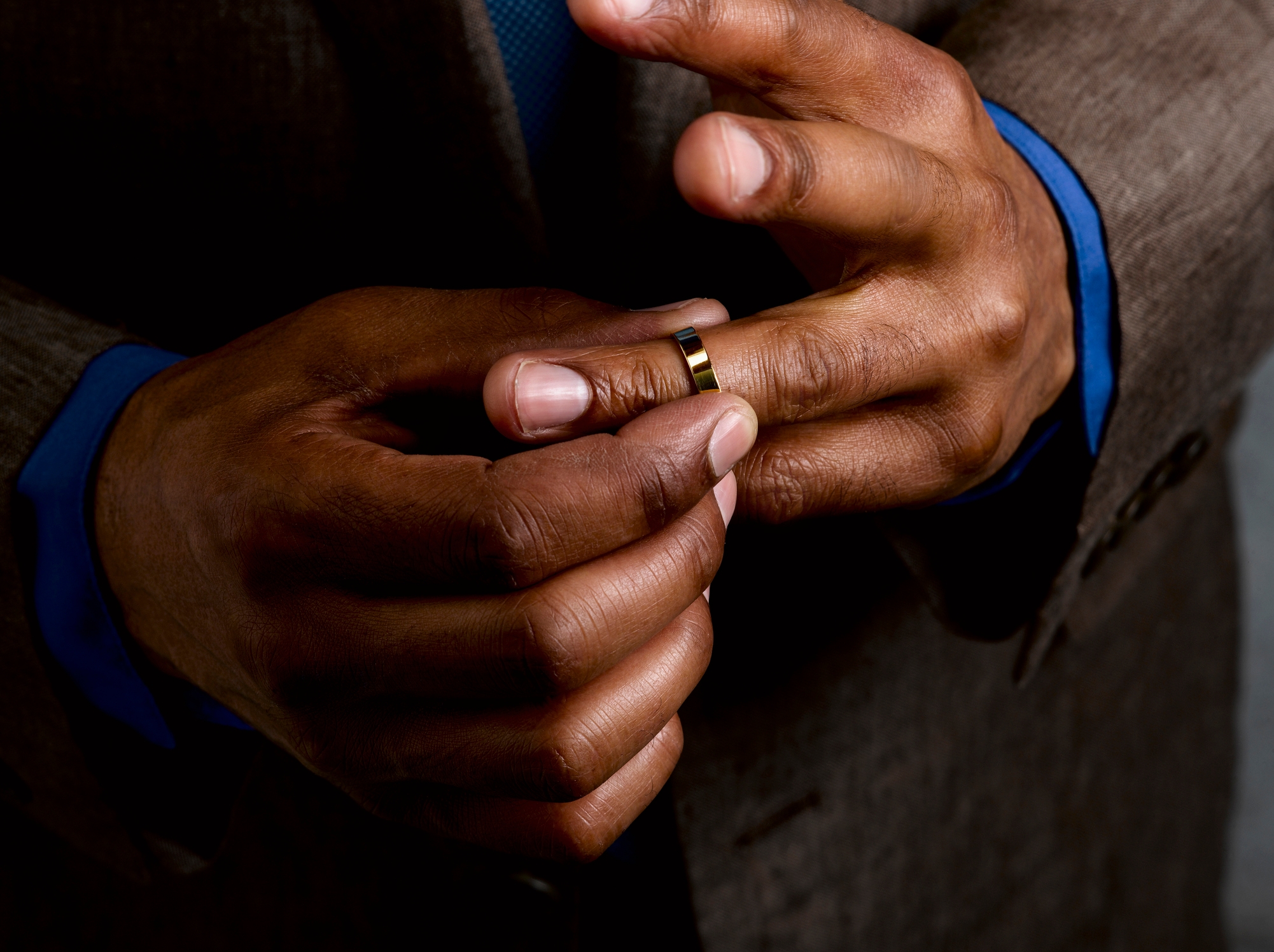 Person in suit adjusts a ring on their finger, focusing on the hands and ring detail