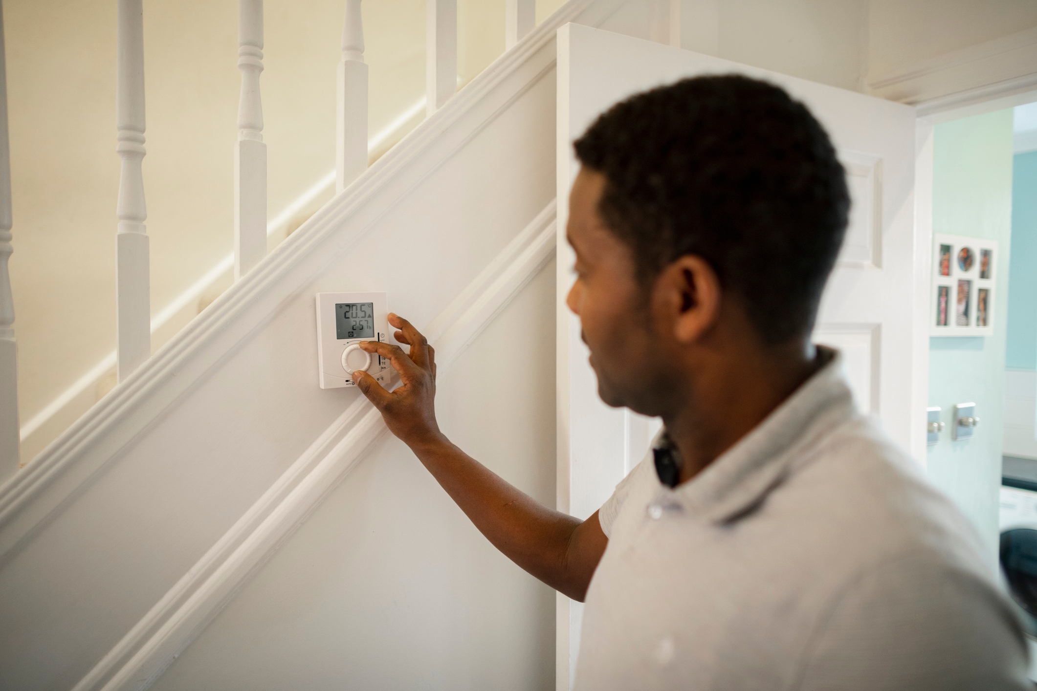 Person adjusting a thermostat on a staircase wall inside a home