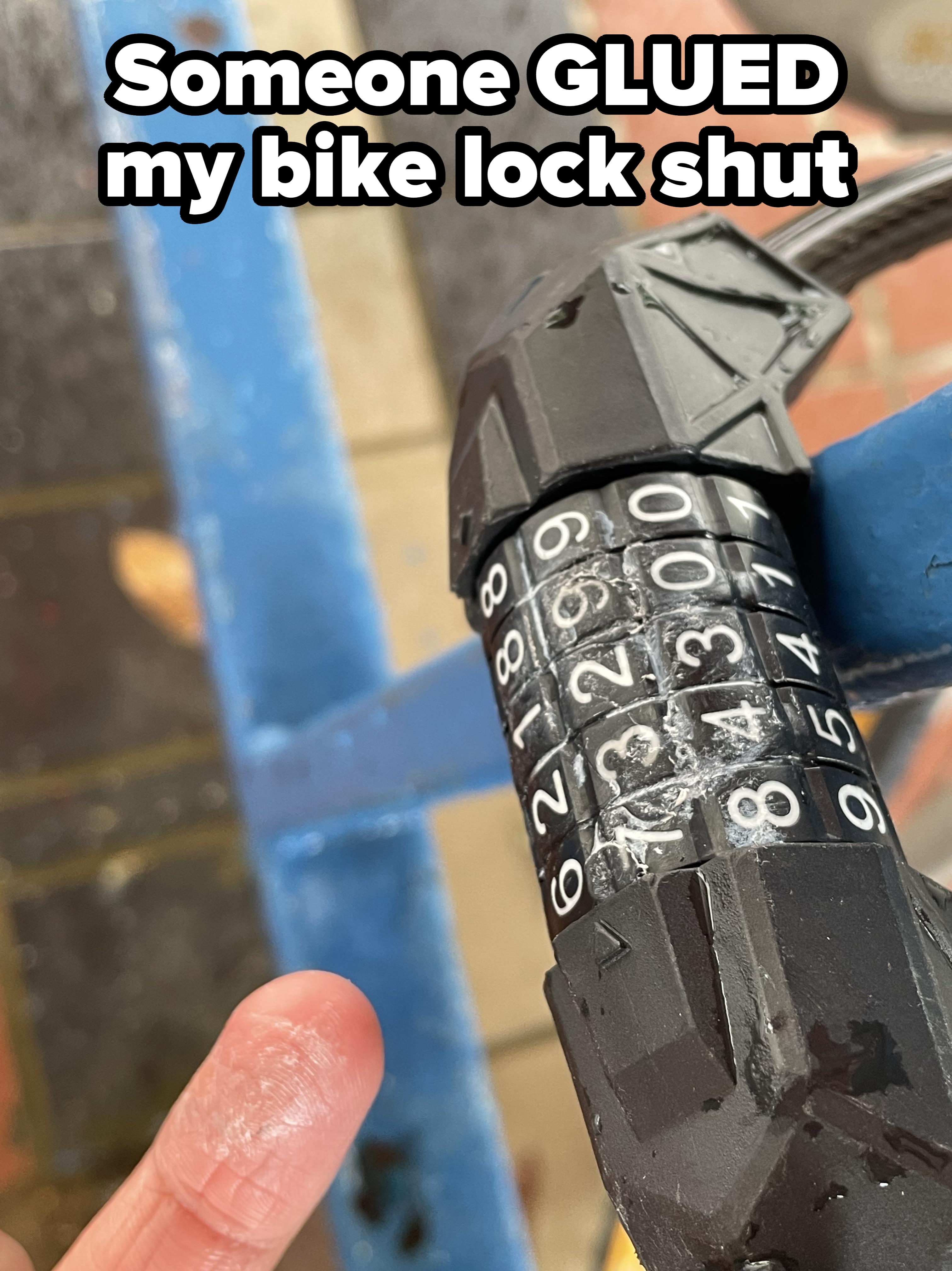 Bike lock with a combination dial showing numbers, damaged casing. Person pointing at the lock