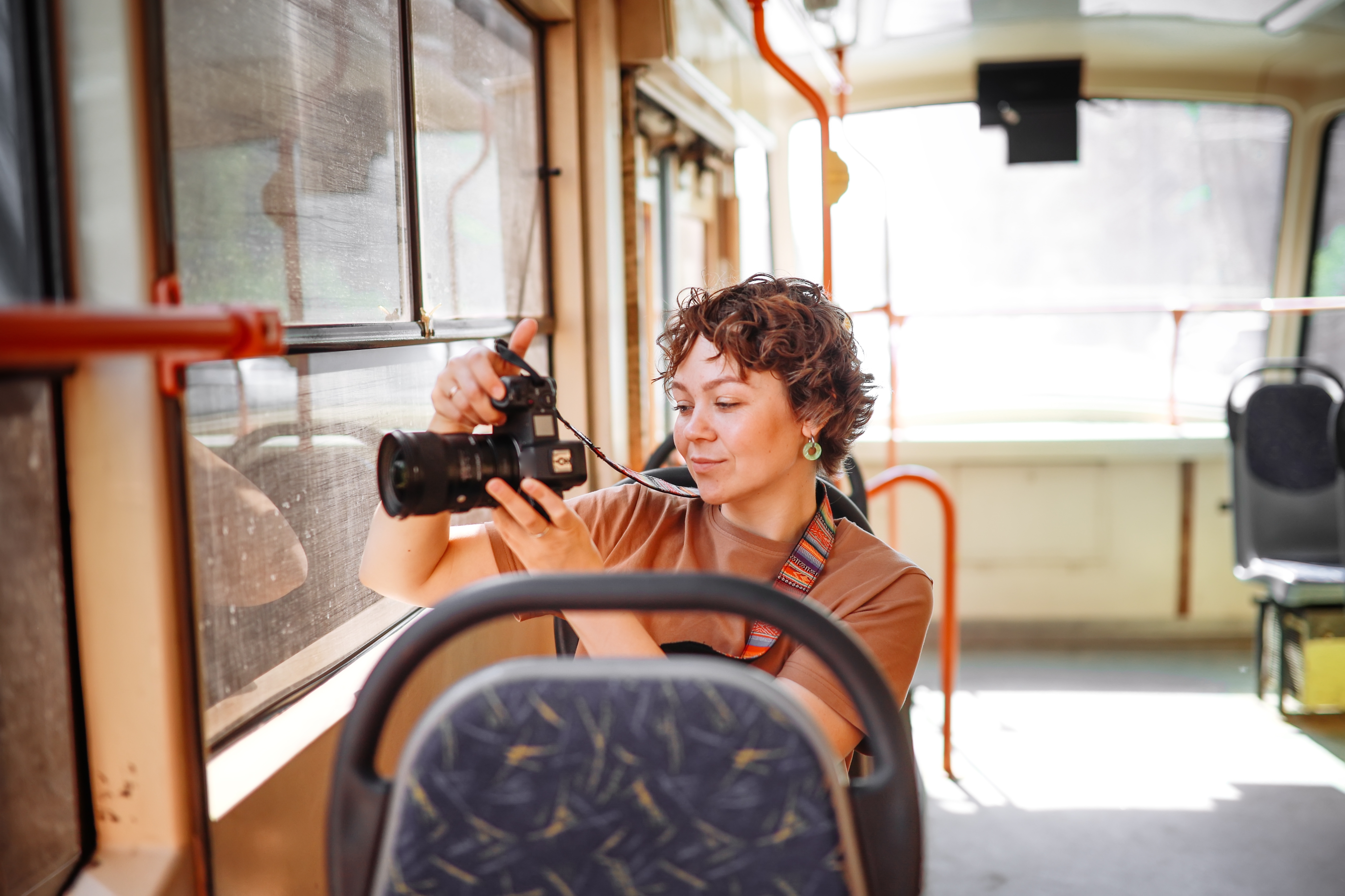 Person in a bus taking a photo with a camera, focusing intently while standing near a window