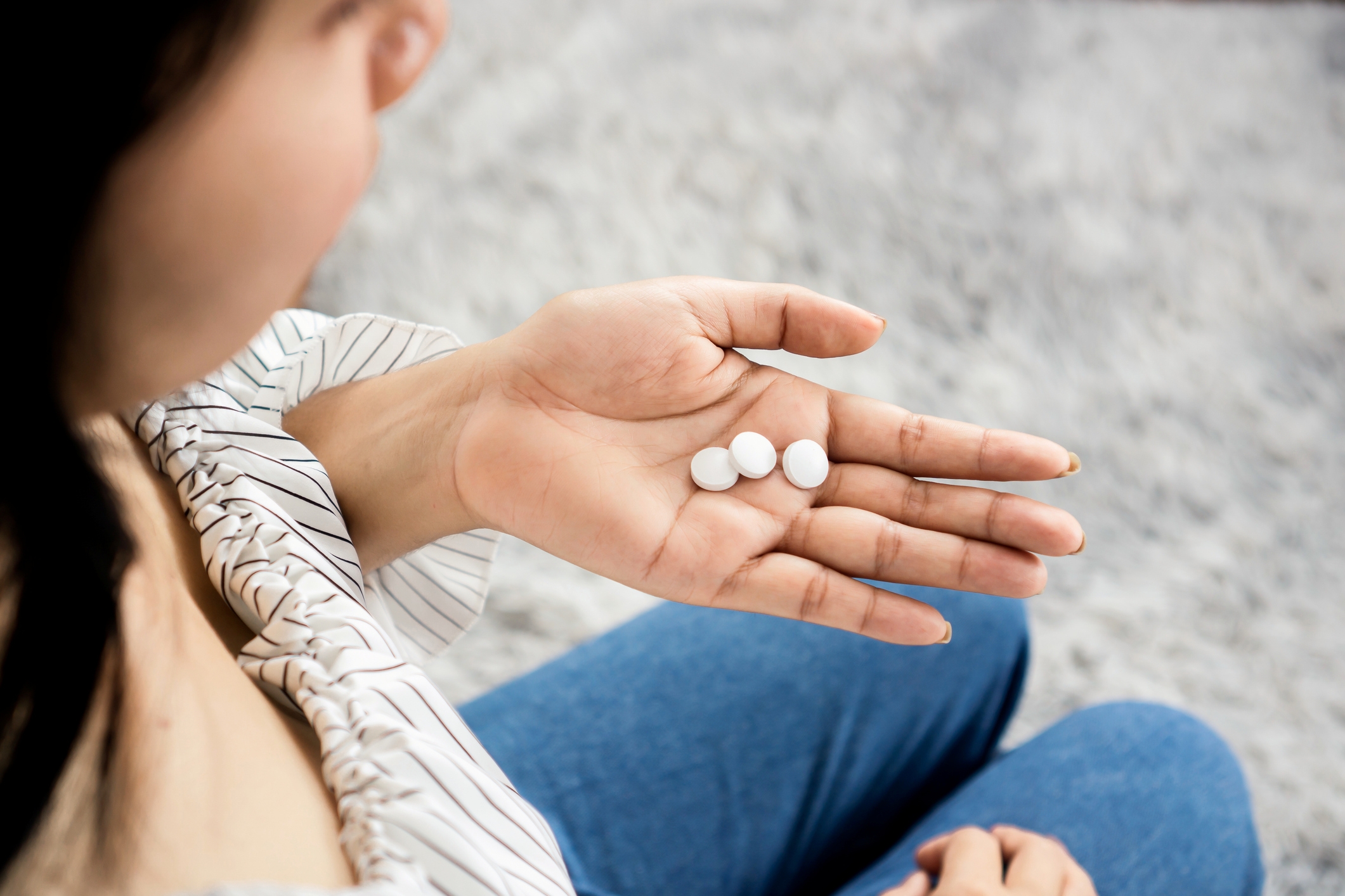Person holding three round tablets in an open hand, wearing a striped top and jeans, seated on a textured floor