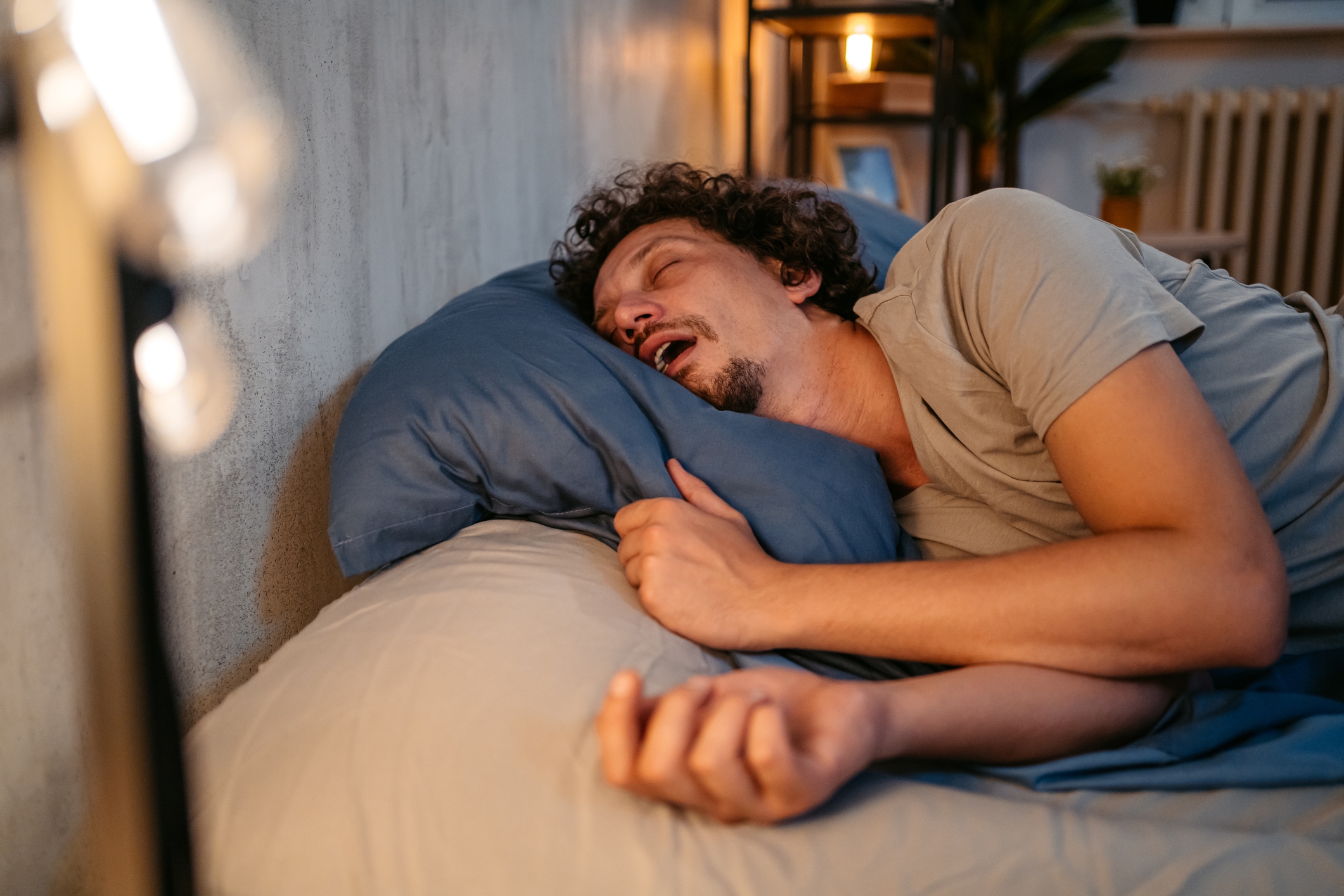 Person sleeping on a bed, mouth open, resting on a pillow in a cozy room setting