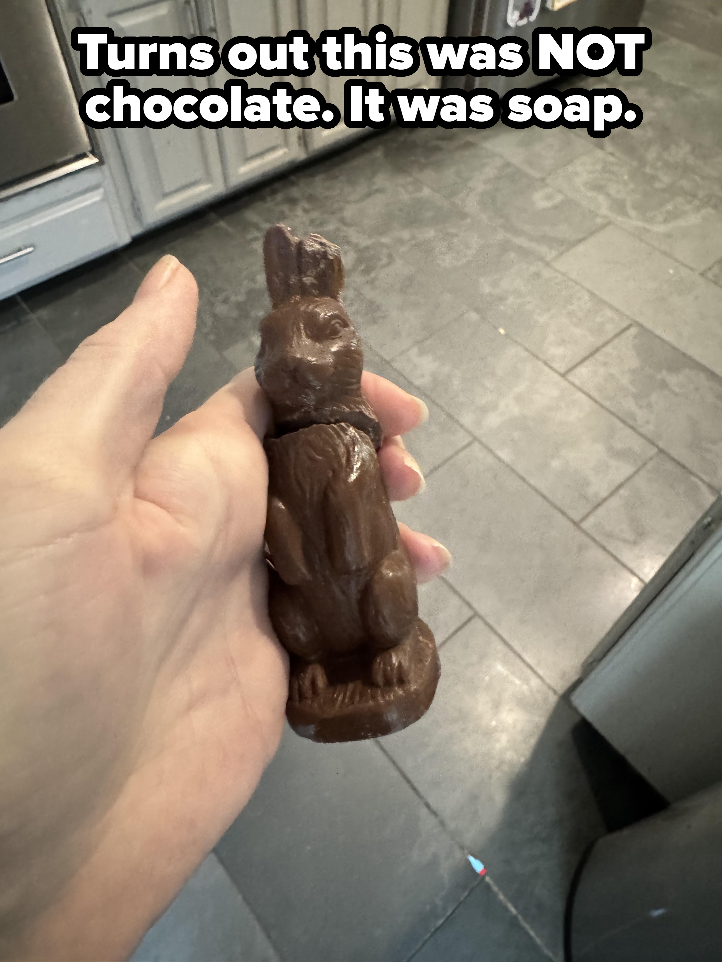 A hand holding a small chocolate bunny on a kitchen floor background
