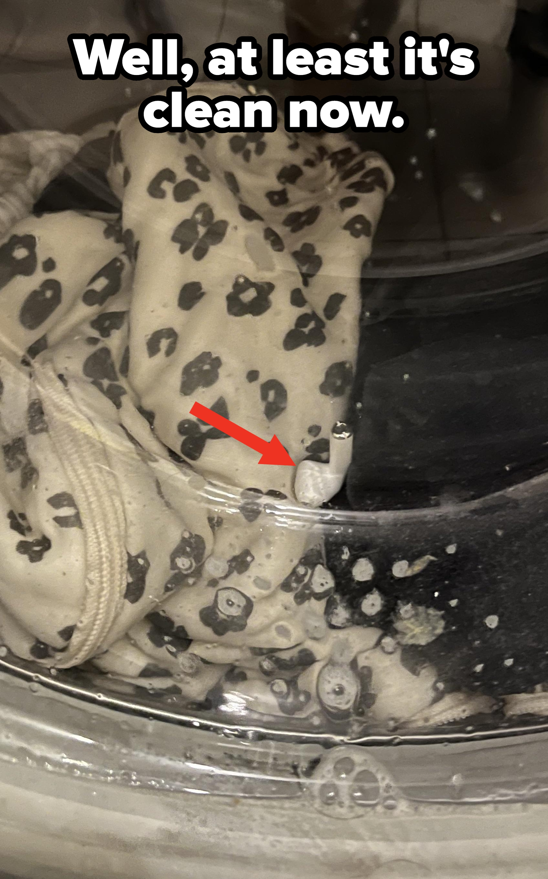 Sweater with a leopard print seen through a washing machine door with soap suds covering parts of the surface