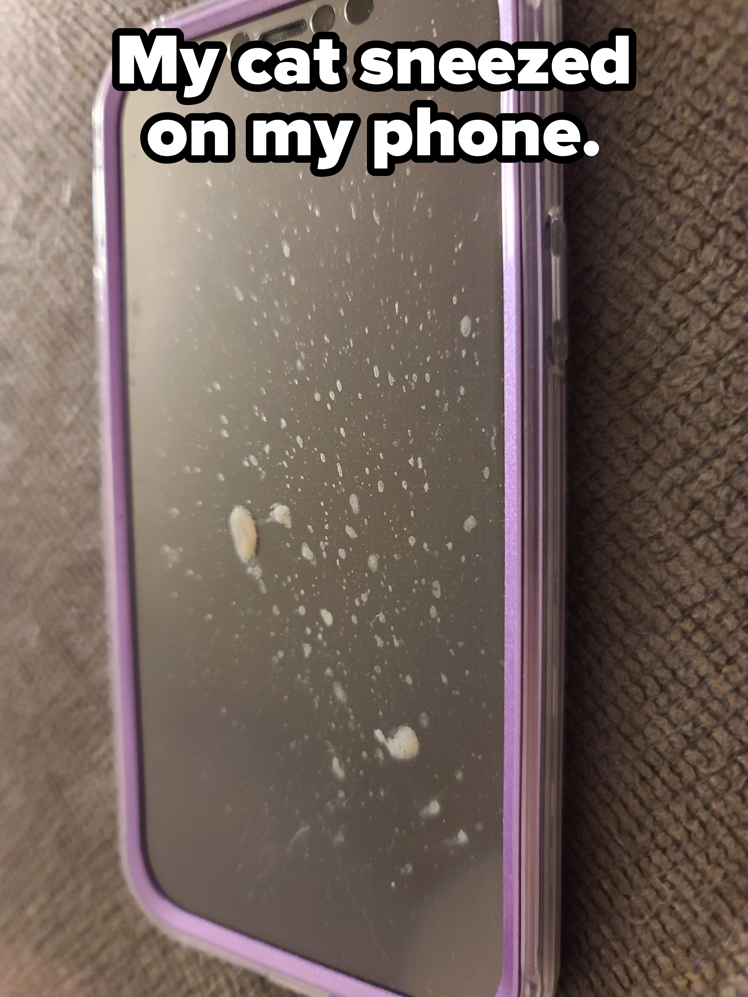 Smartphone with a purple case, screen covered in white droplets, lying on a fabric surface