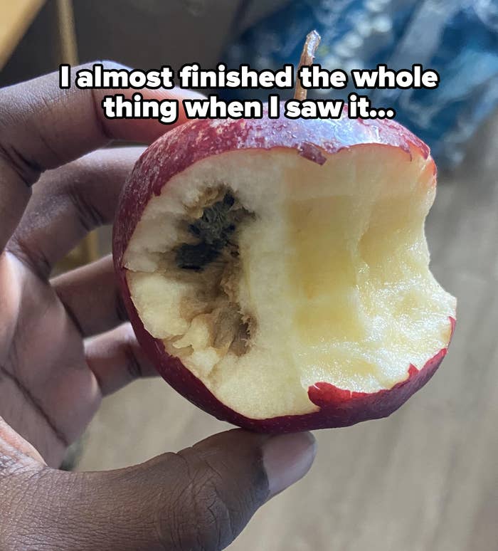 A person holds an apple with a large bite and visible rot on one side