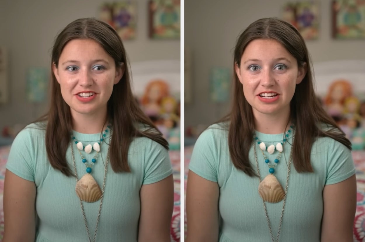 A cast member from "Love On The Spectrum" in a room, wearing a light short-sleeve top and layered necklaces with shells. They're sitting in front of a bed with colorful decor