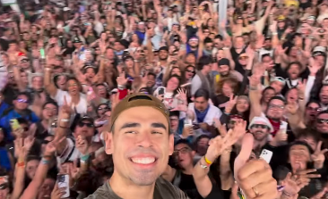 Person taking a selfie with a large, enthusiastic crowd at a music festival, arms raised in excitement