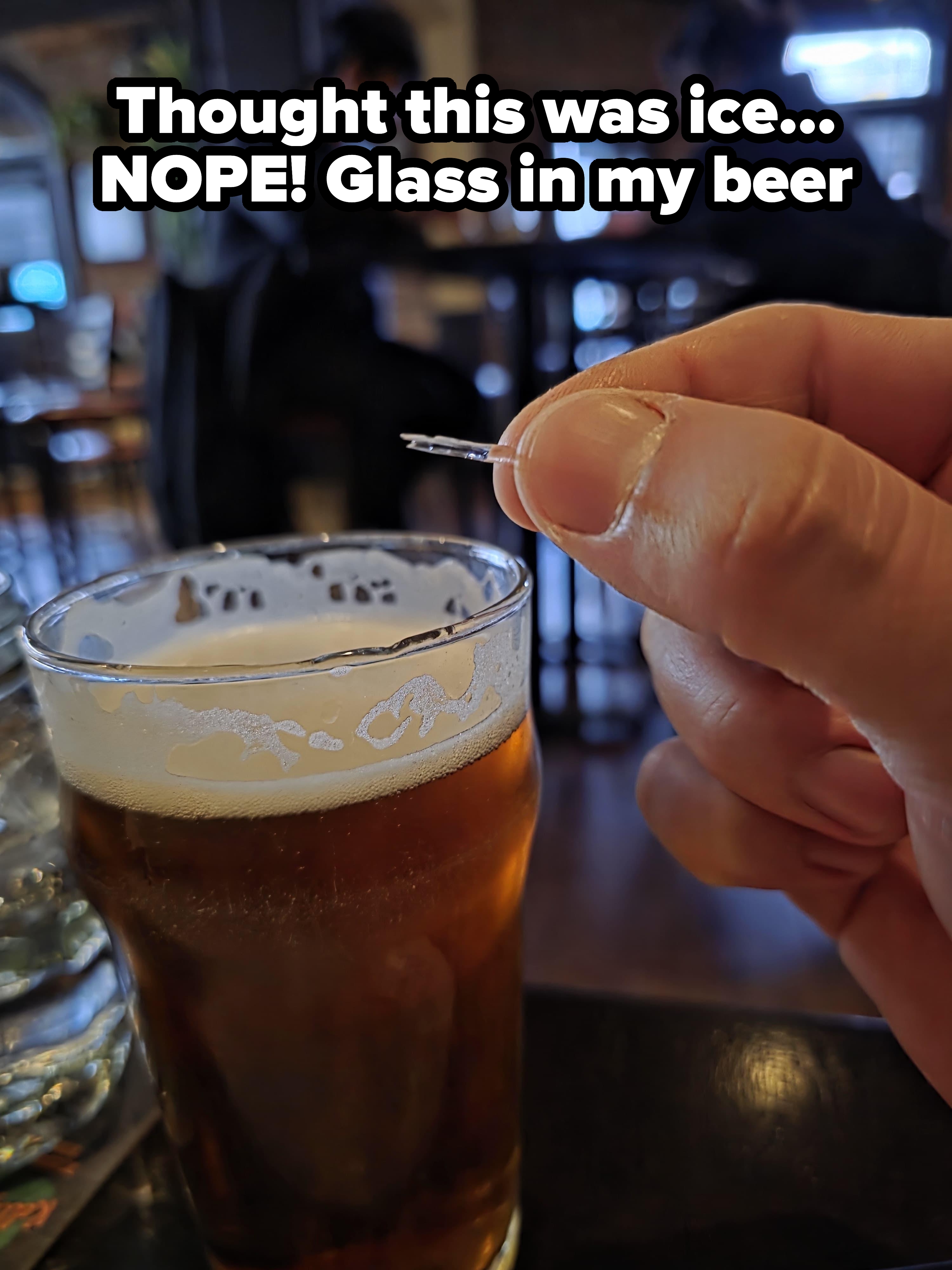 A hand holding a small fish bone next to a pint of beer in a casual dining setting