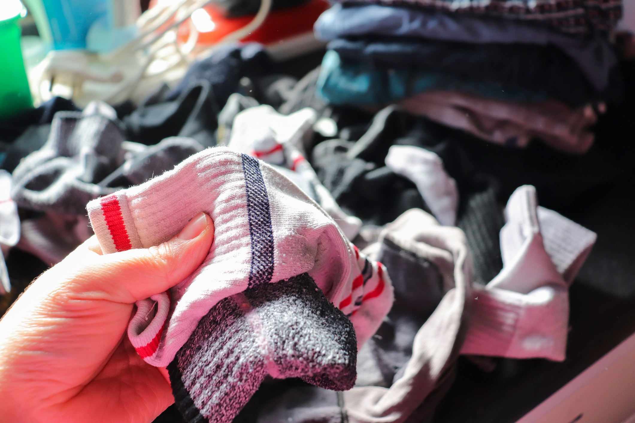 A hand holds mismatched socks, with more socks in the background, suggesting a routine laundry task
