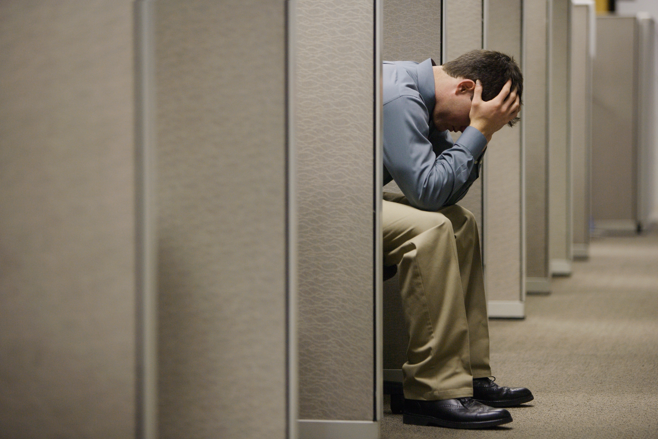 Person sitting in an office cubicle, holding their head in their hands, appearing stressed or worried