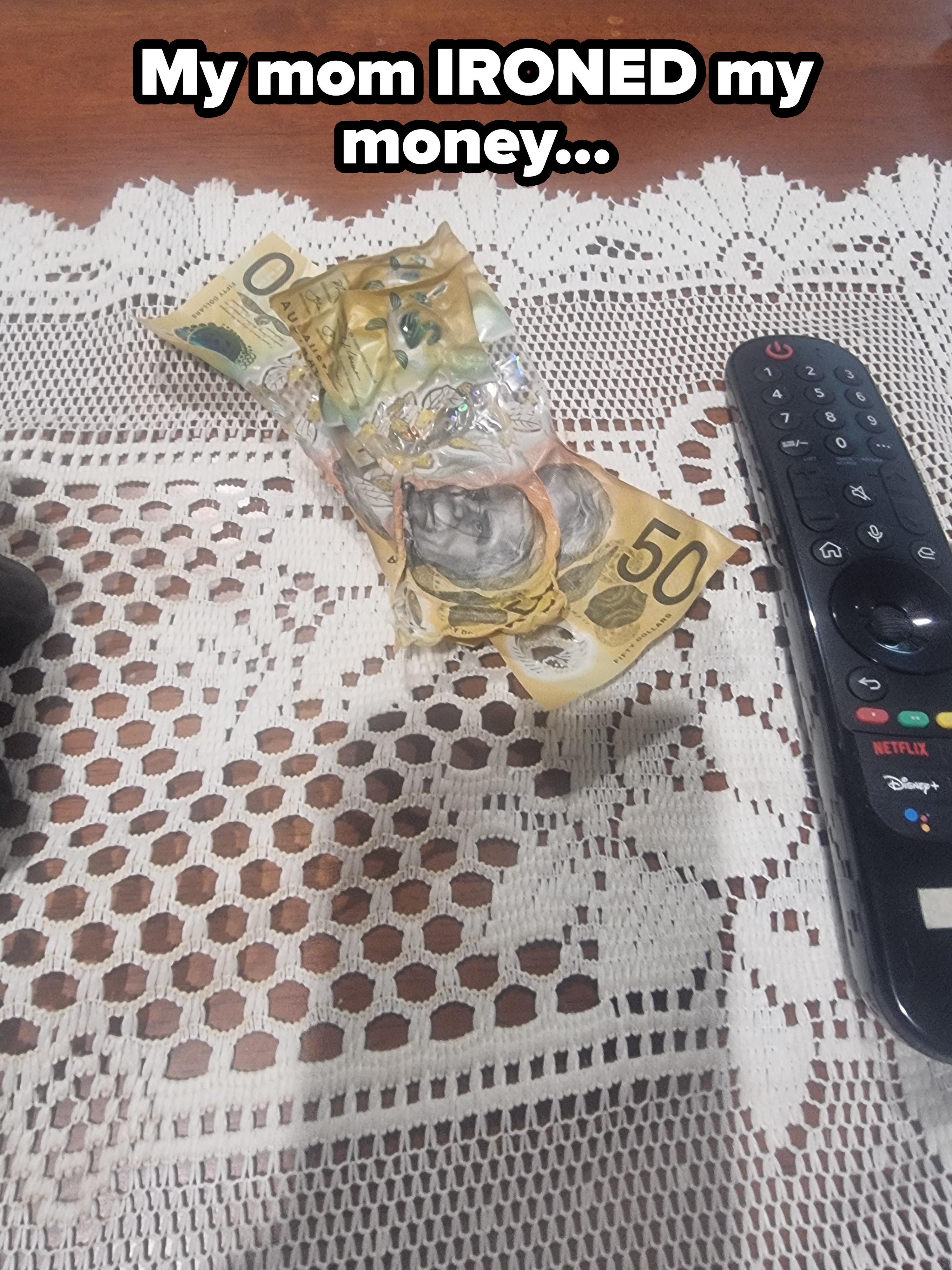A melted remote with Australian currency stuck inside, placed on a lace tablecloth
