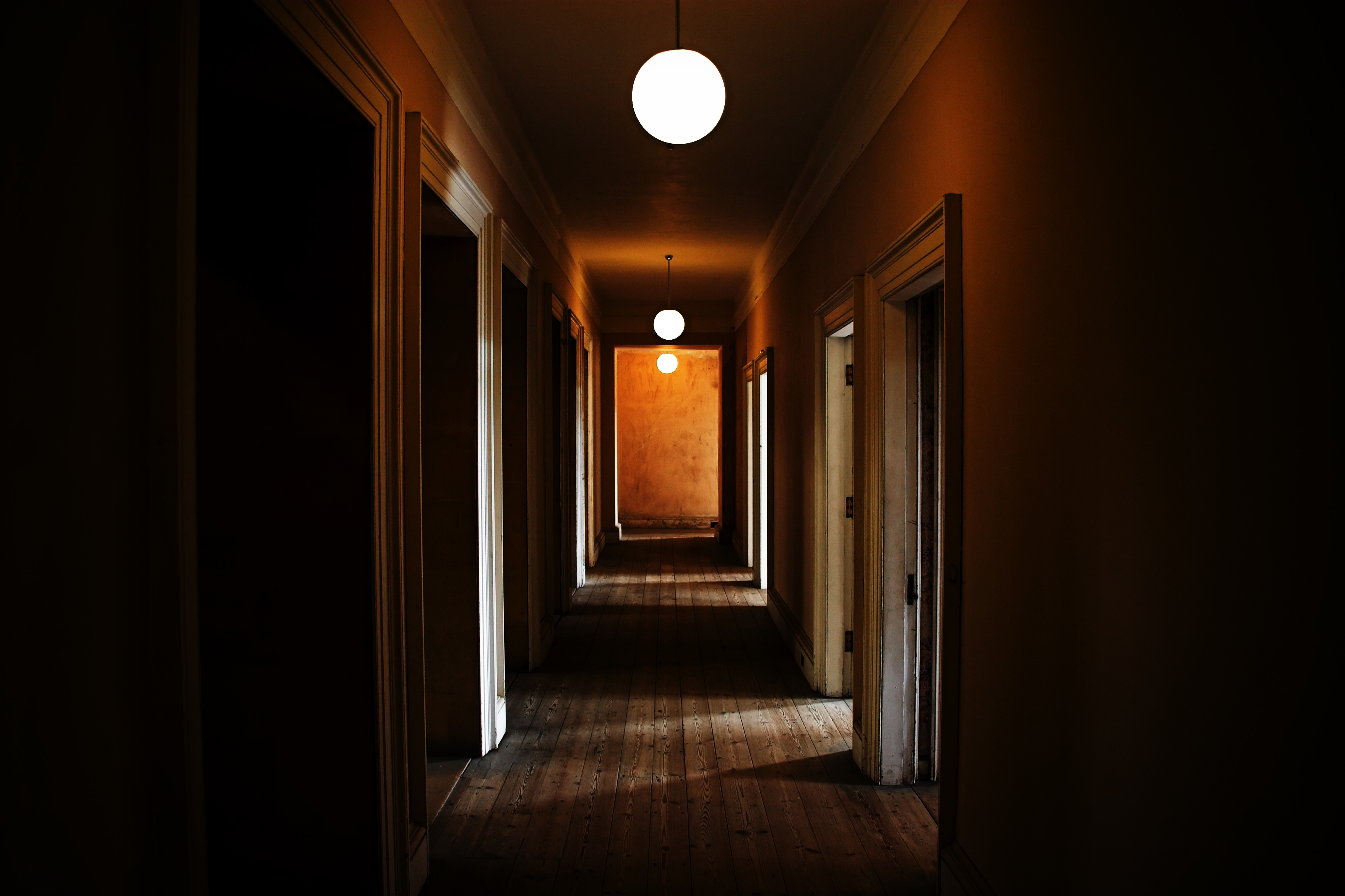 Dimly lit, long hallway with closed doors on both sides and round ceiling lights, creating a mysterious atmosphere