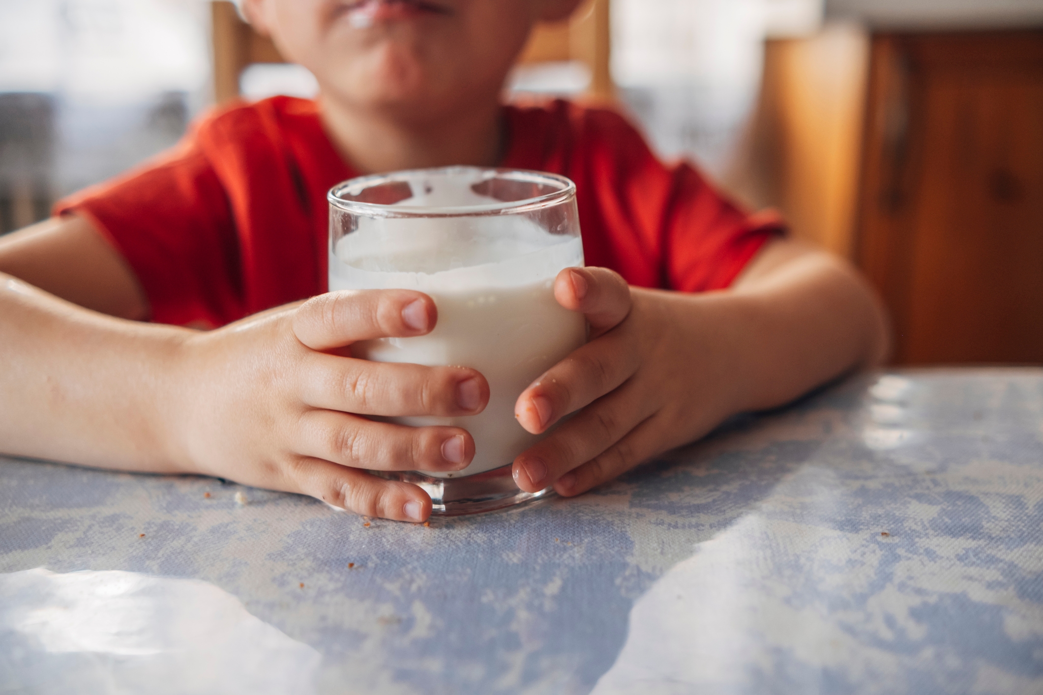 Child holding a glass of milk with both hands, sitting at a table