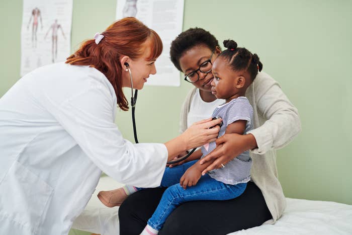 Doctor uses stethoscope on child sitting on parent's lap in a doctor's office