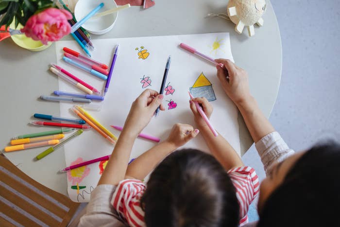Child and parent drawing together at a table with markers and paper, creating colorful artwork with shapes and butterflies
