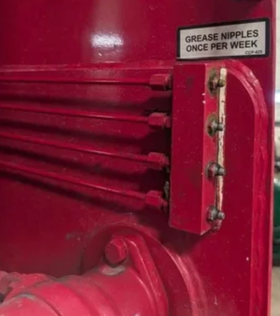 Mechanical equipment with a label reading "Grease nipples once per week."