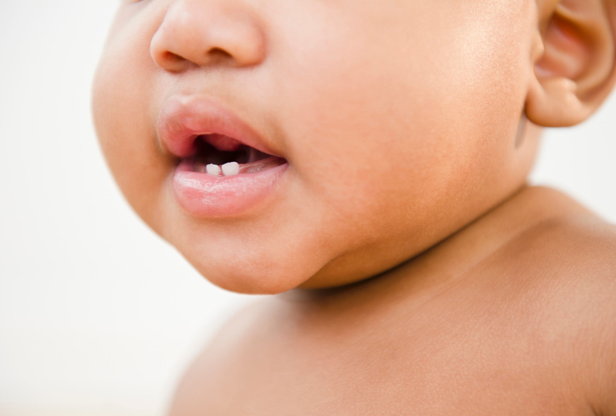 A close-up of a baby's face showing the mouth with a small tooth visible in the lower gum
