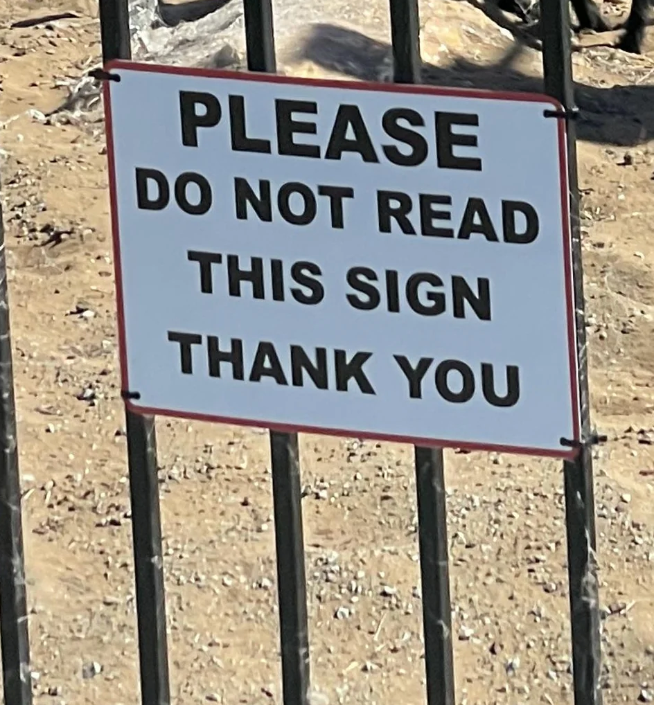 Sign on a metal fence reads: "Please do not read this sign. Thank you."