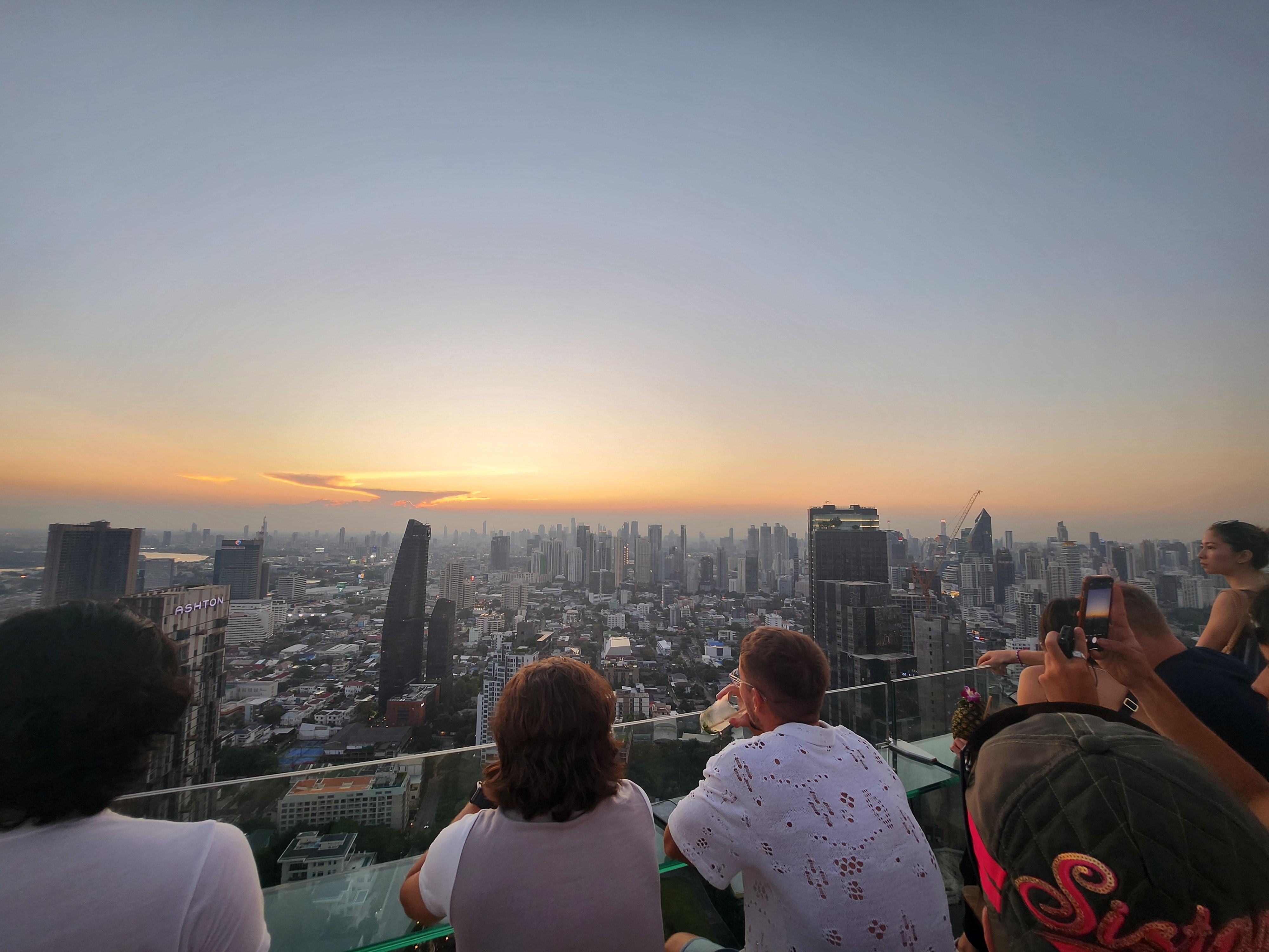 People enjoy a cityscape from a rooftop at sunset. The focus is on relaxation and leisure in an urban setting, fitting the Work &amp;amp; Money theme