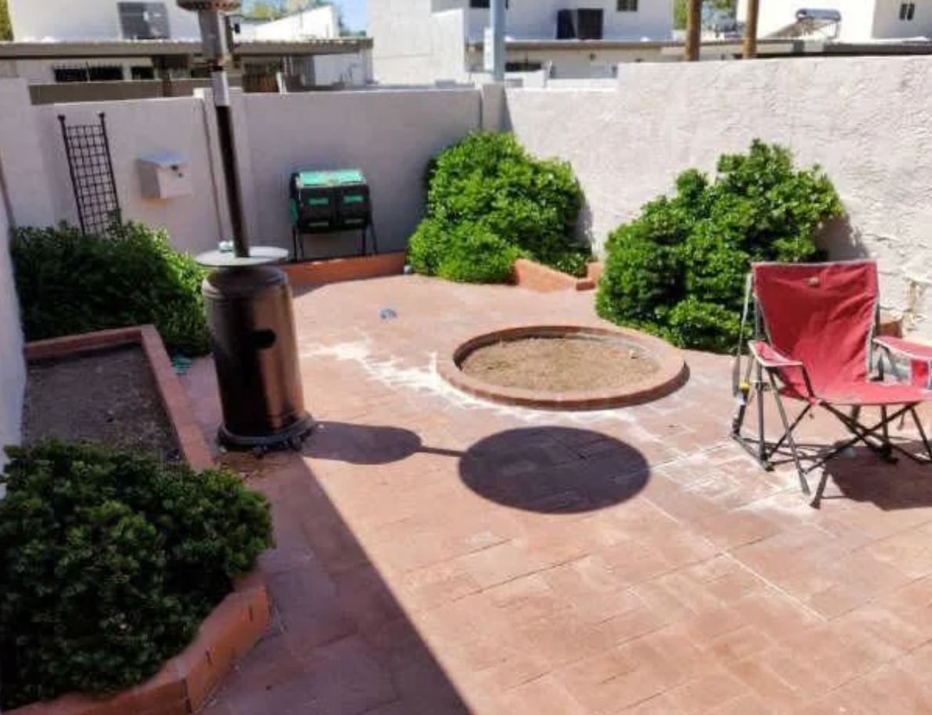 Small patio with a fire pit, folding chair, and plants against the wall. A patio heater stands beside the fire pit