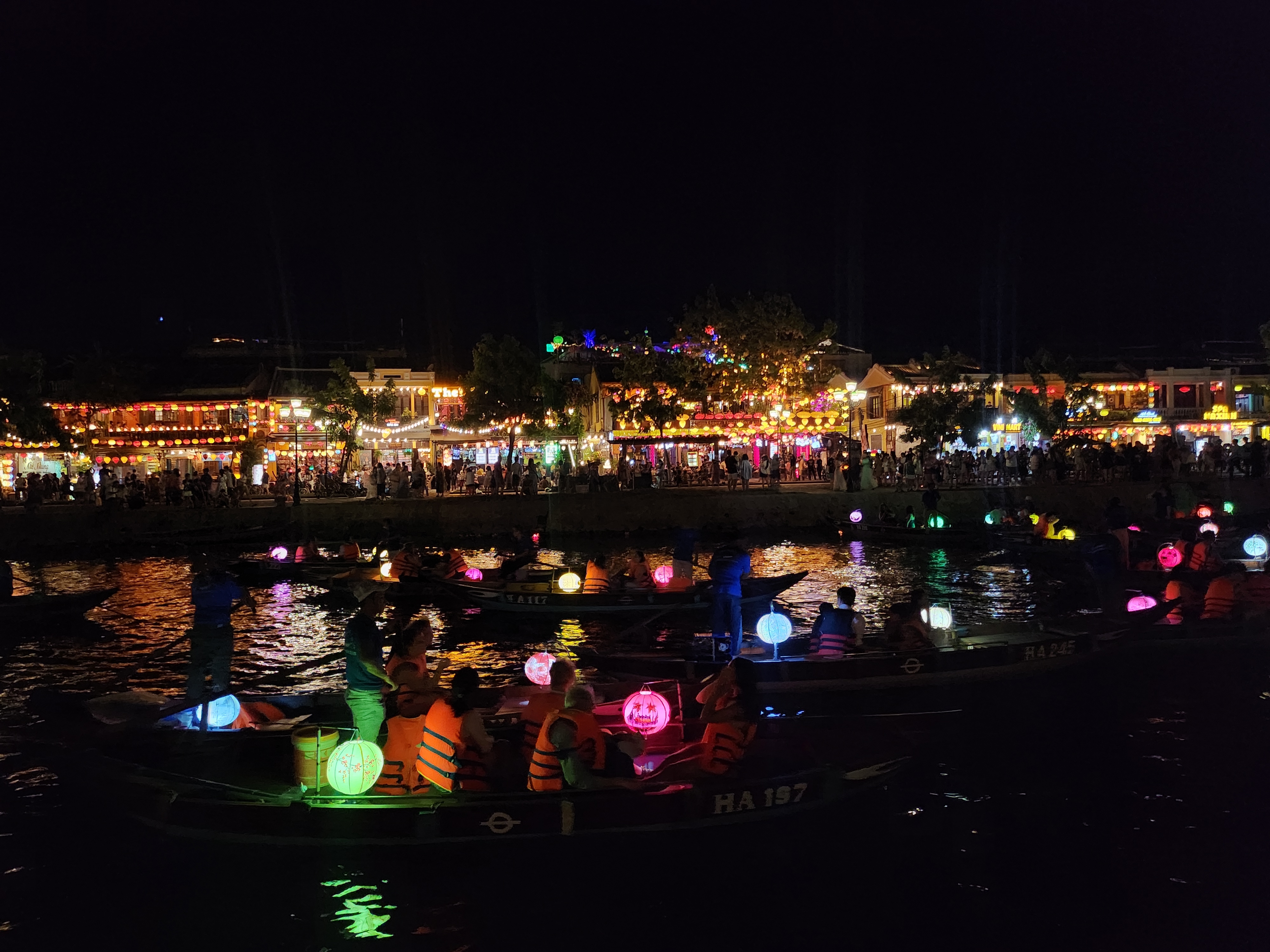 People in boats with colorful lanterns at a lively nighttime riverside festival