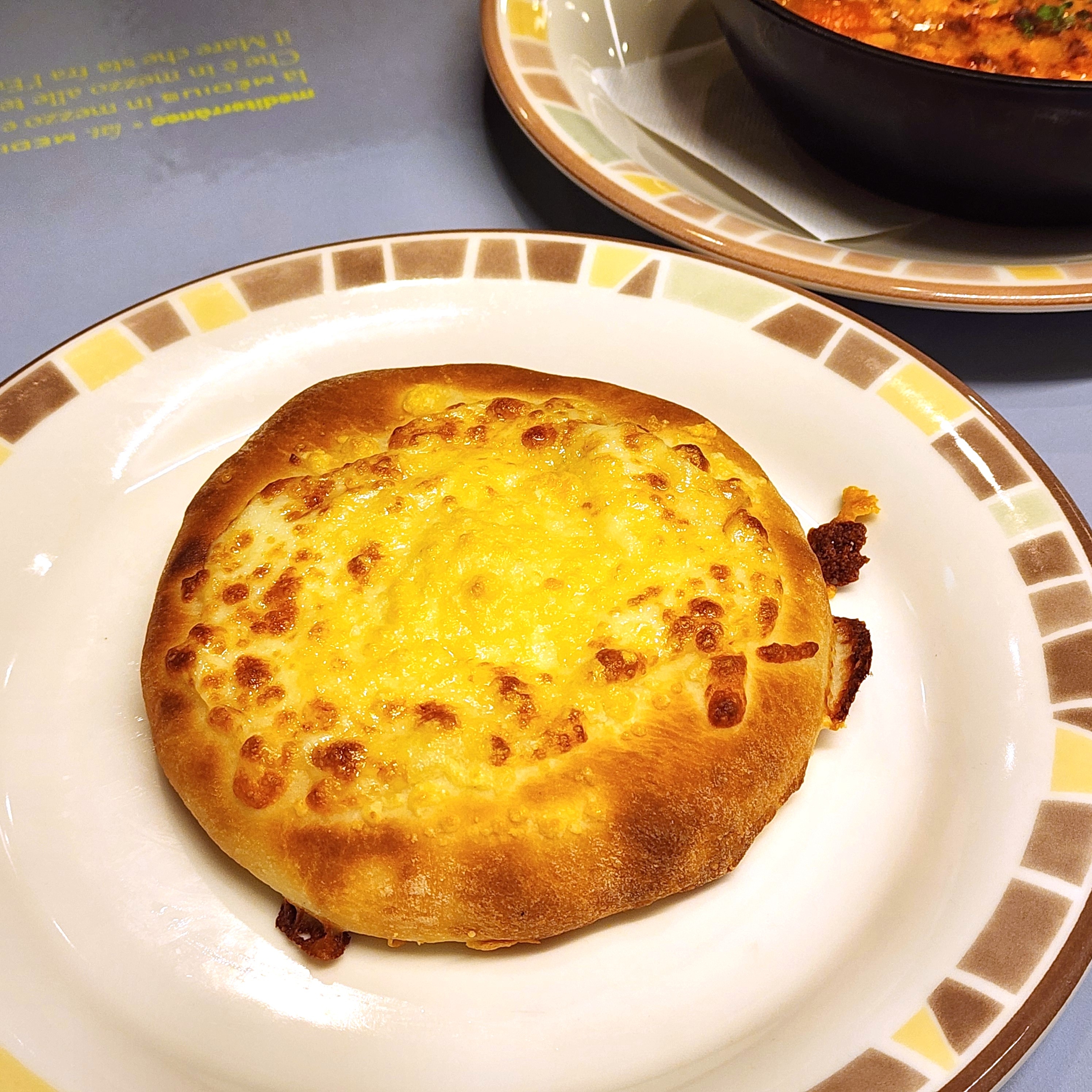 皿に乗った焼きたてのチーズパン。背景には別の料理が少し見える。