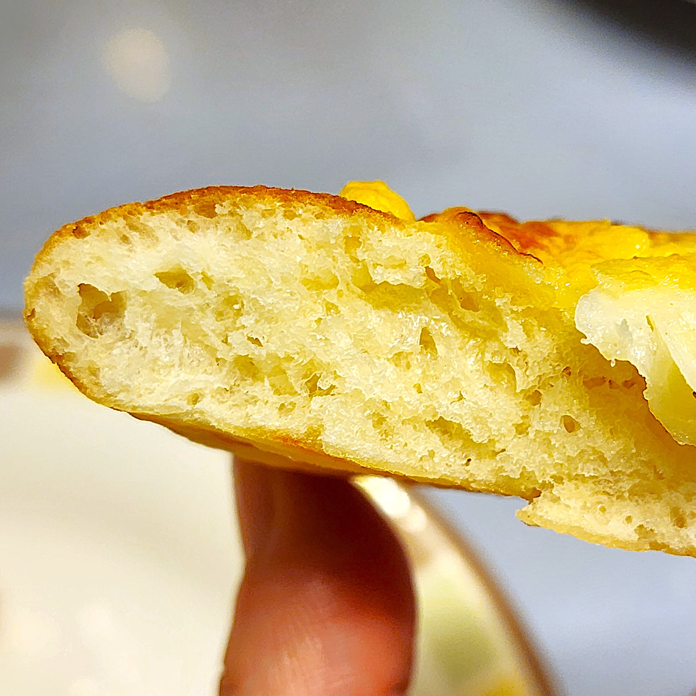 手に持たれたピザの一部。ふんわりした生地と溶けたチーズが見える。