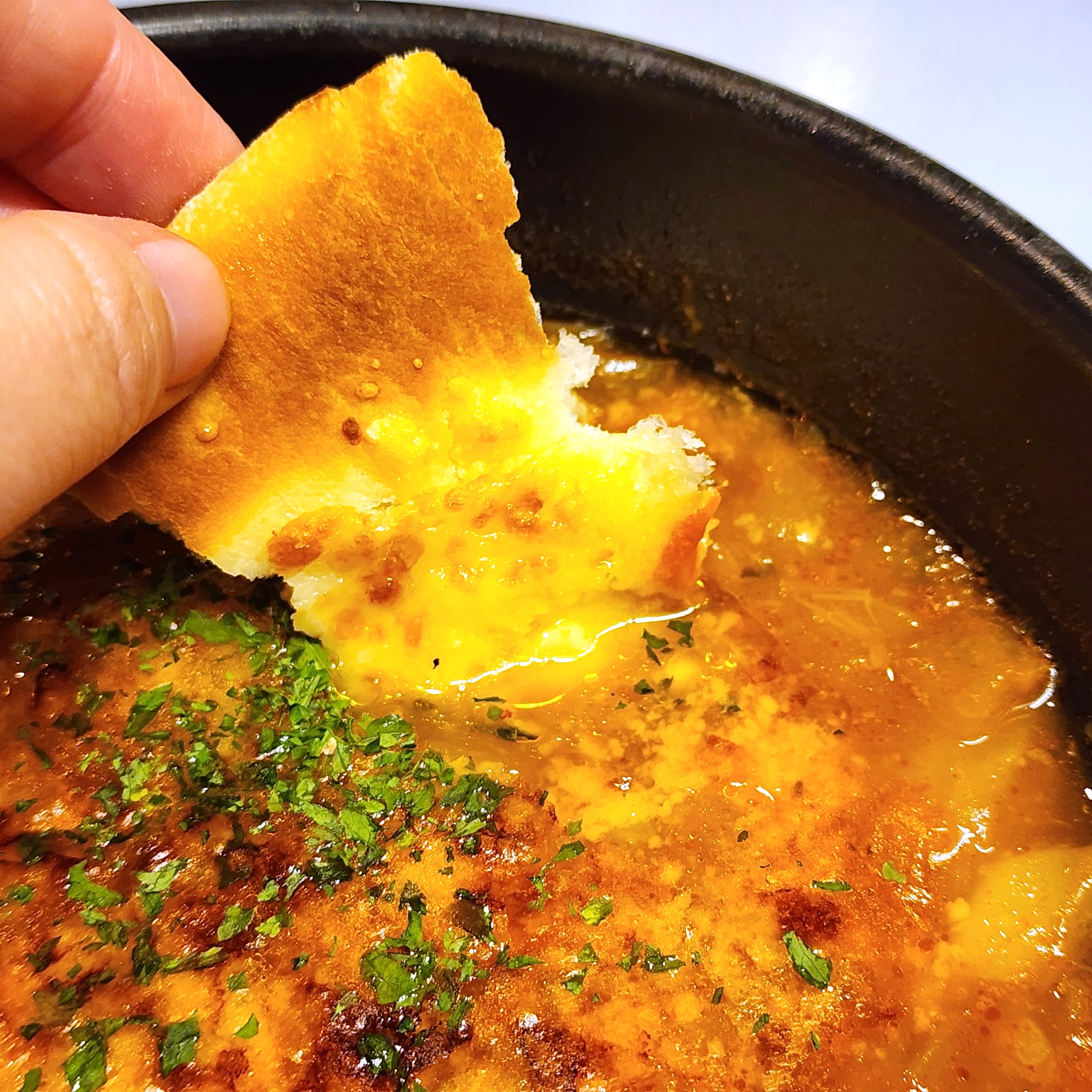 手がパセリのかかった濃厚なスープにパンを浸しているシーン。