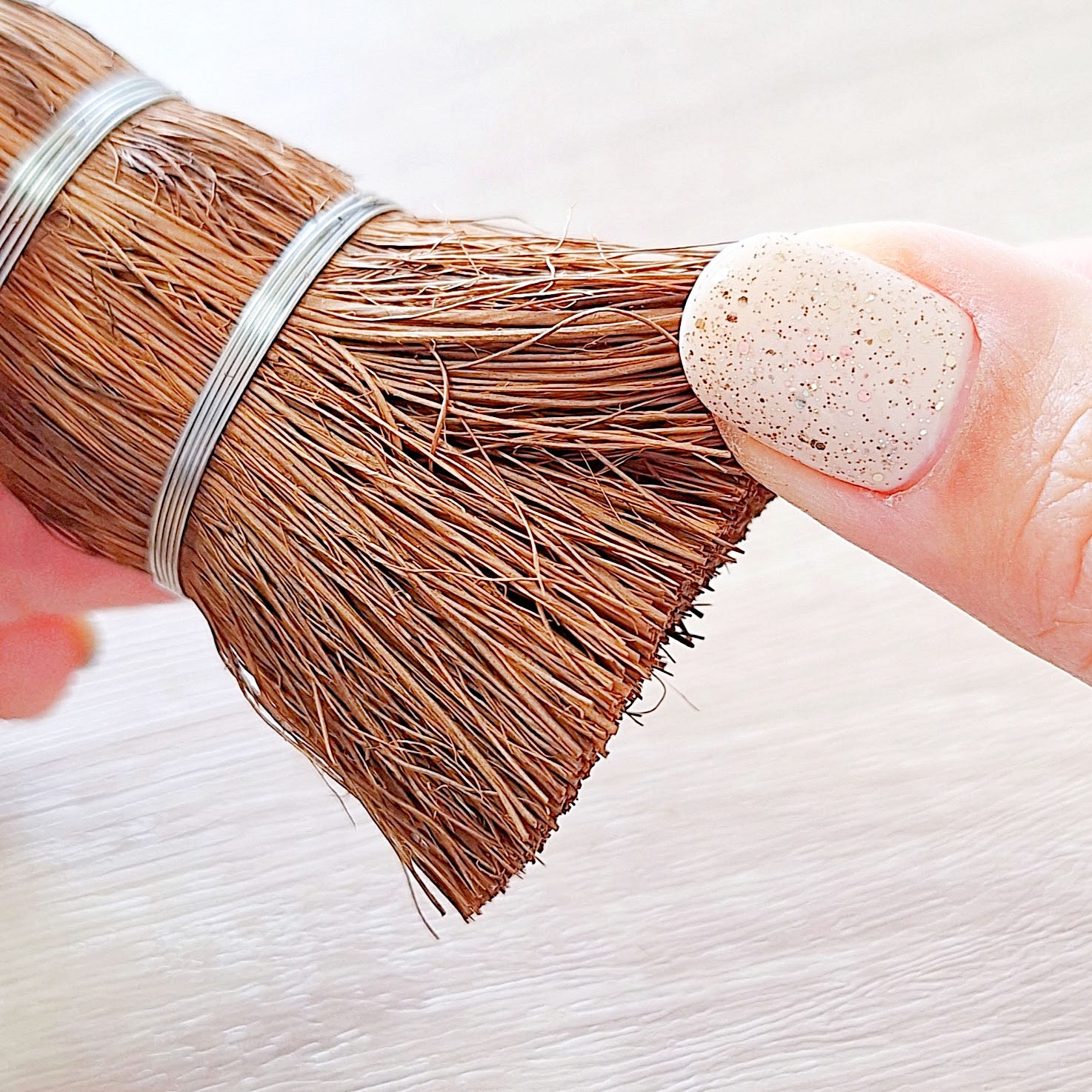 手に持たれた木製のブラシの先端。指のネイルは白で、微細な模様が施されている。