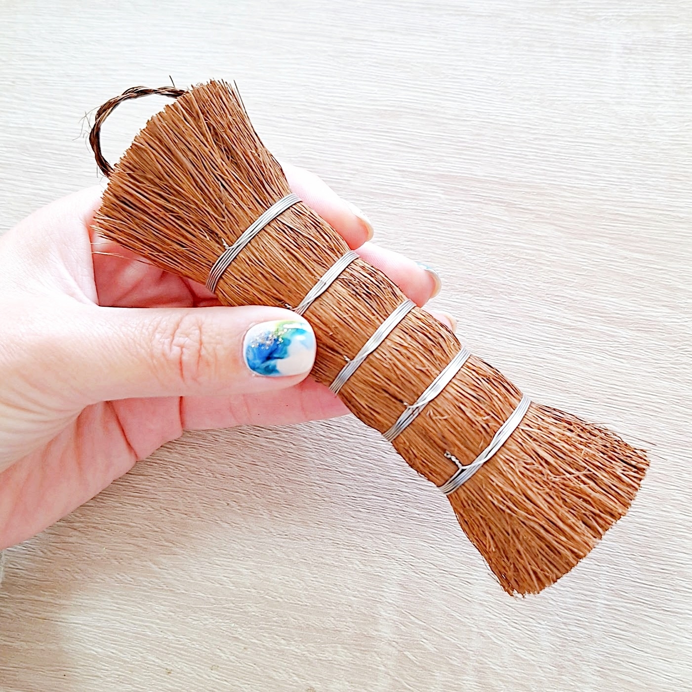 手で持った小さな手織りほうき。シンプルなデザインで、自然な素材が使用されています。