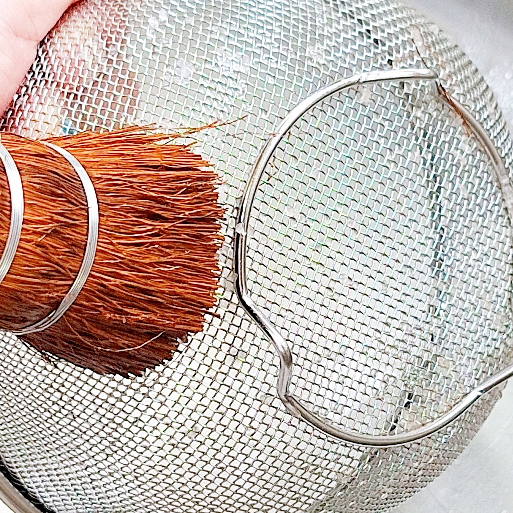 手が大きな筆を使って金属製の道具を掃除している様子。