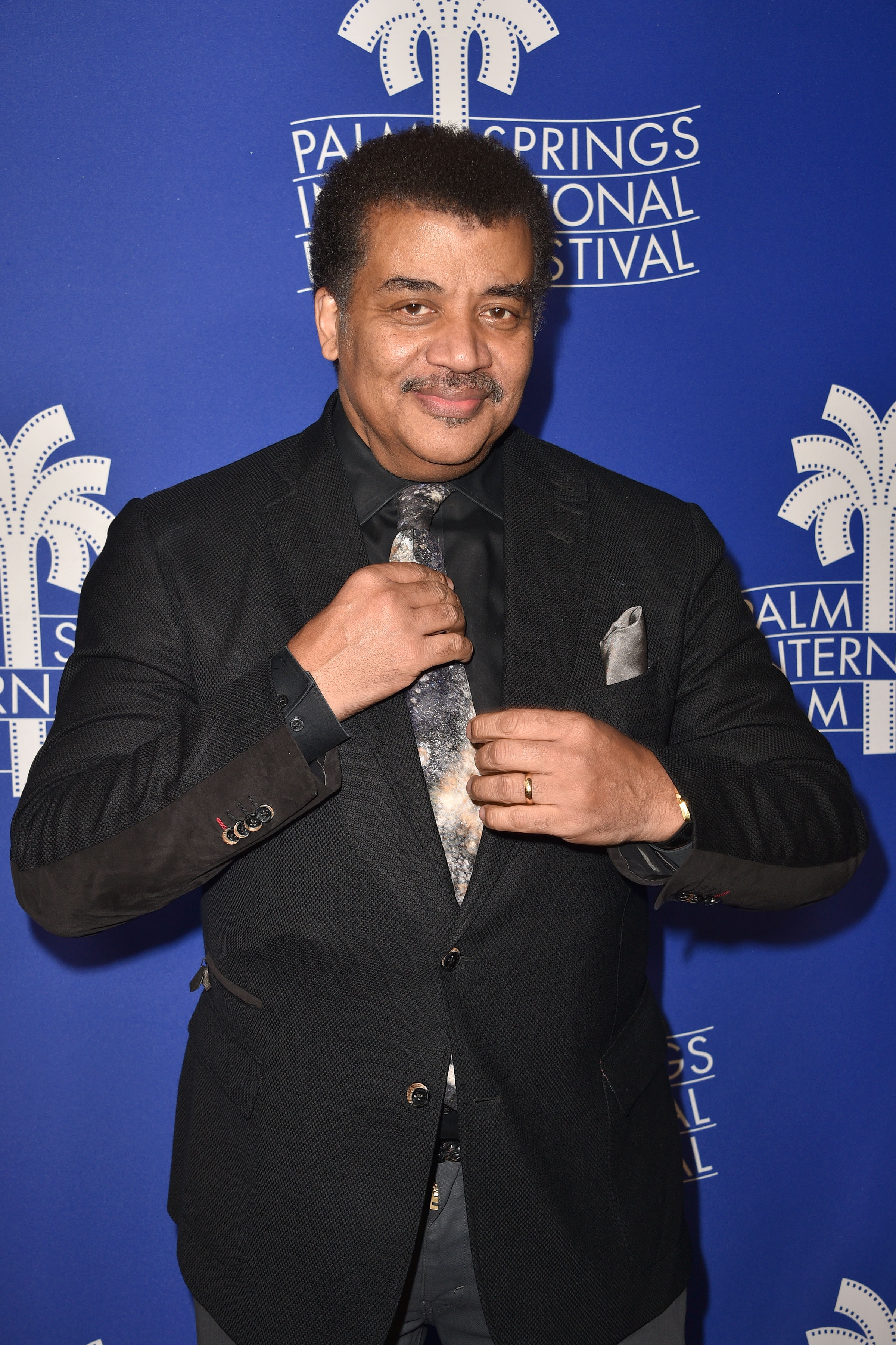 Person in a suit adjusting tie at Palm Springs International Film Festival backdrop