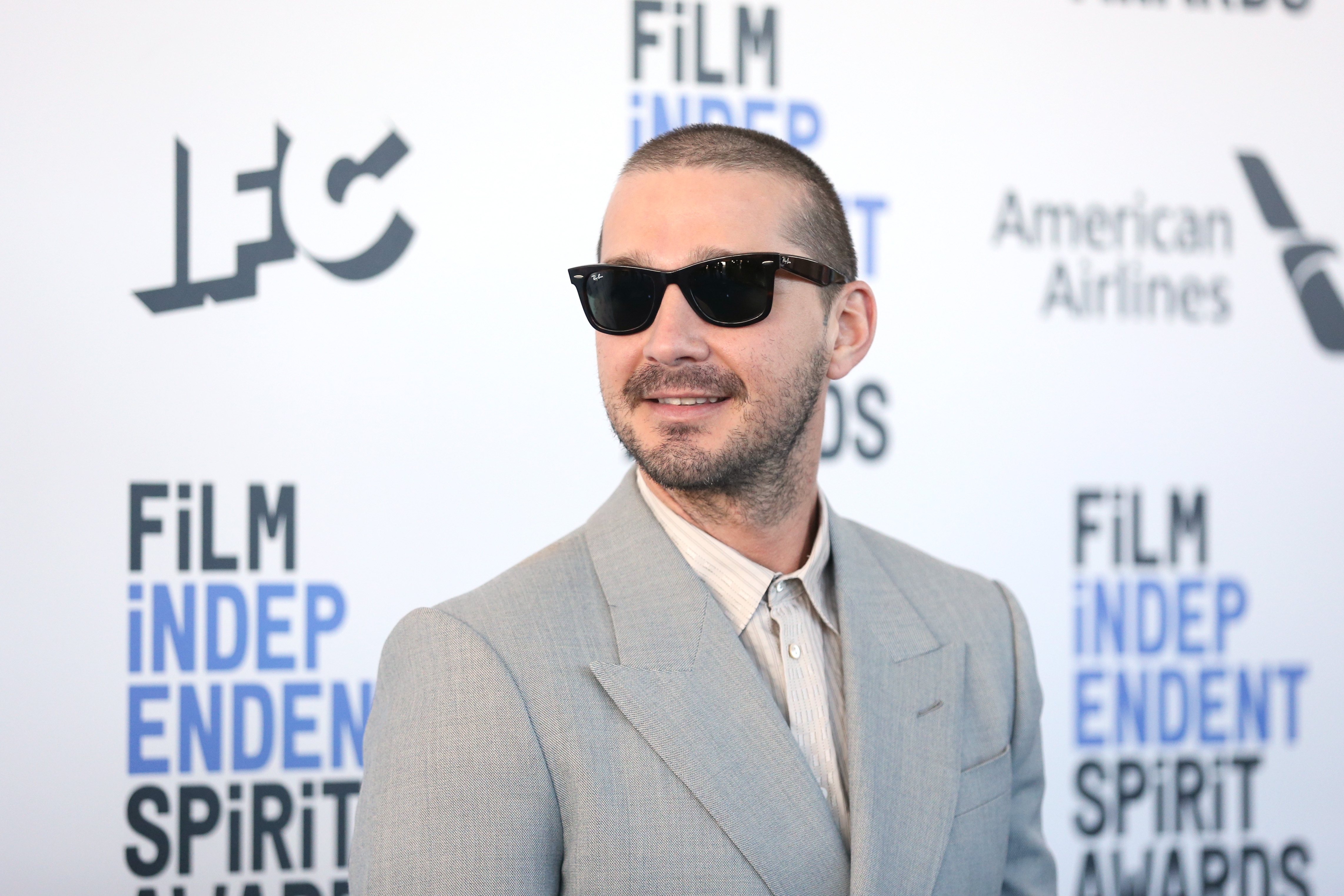 Person in a light suit and sunglasses at a Film Independent Spirit Awards event backdrop