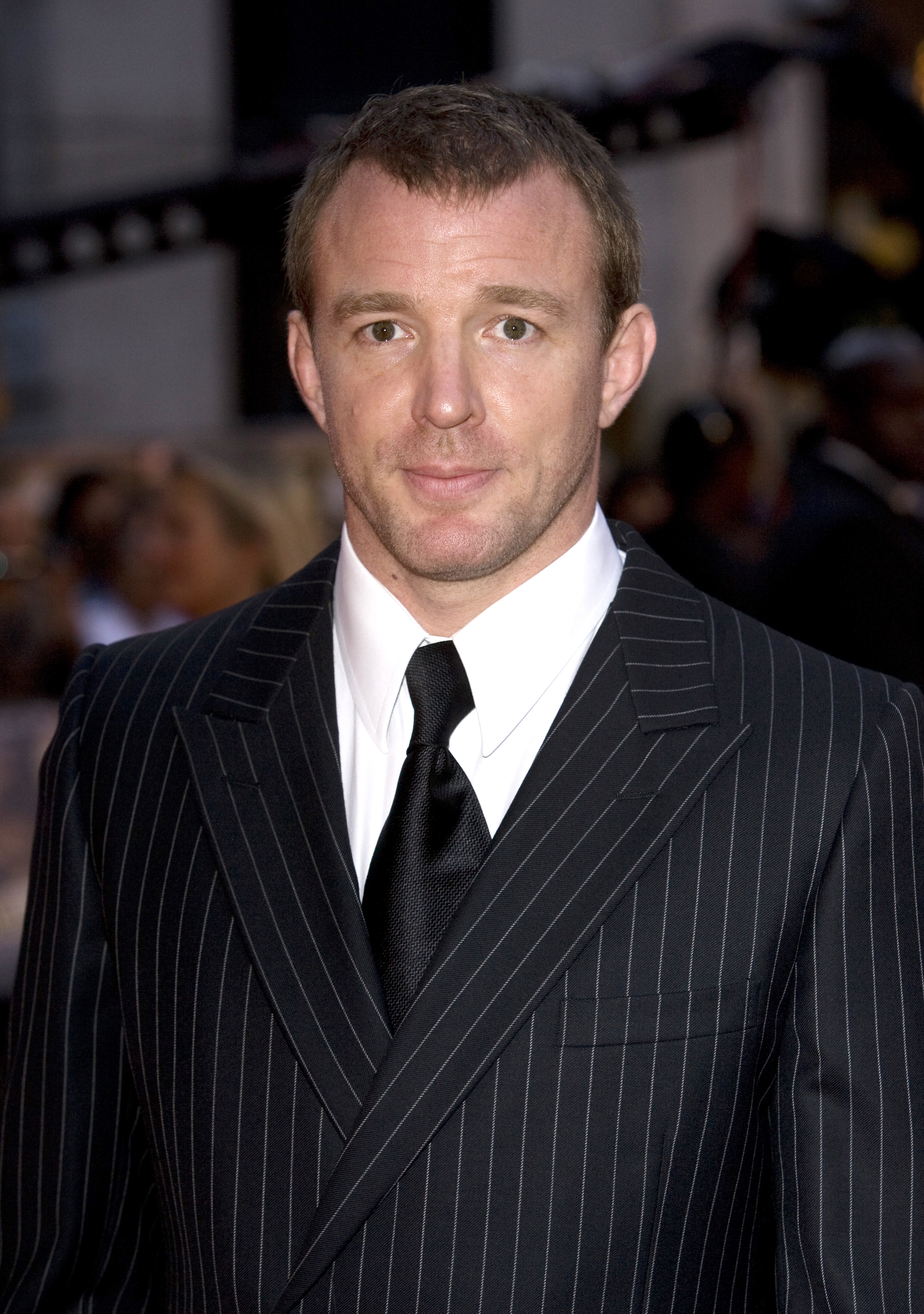 Person on a red carpet in a pinstripe suit and tie, attending a formal event