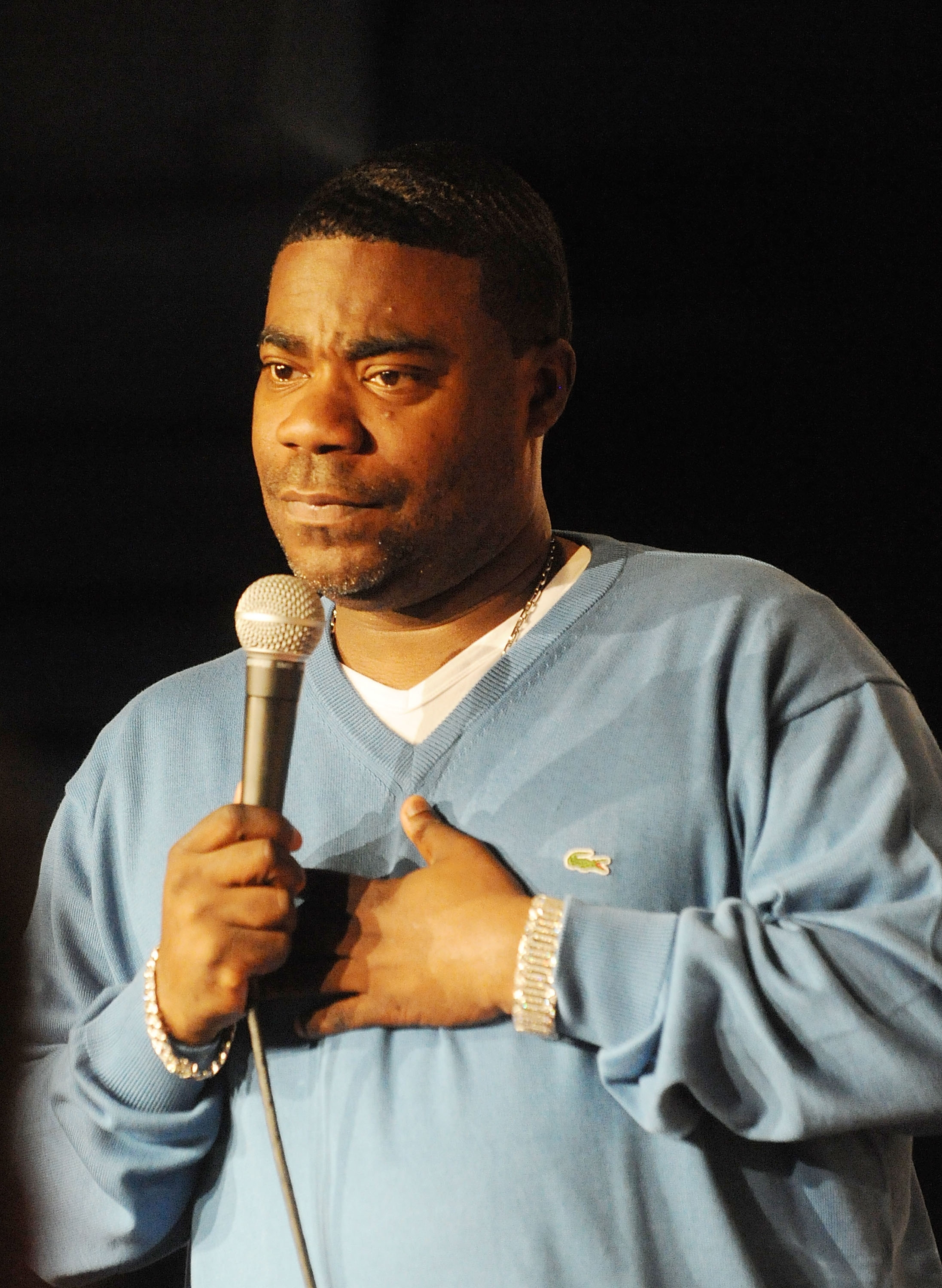 Person on stage holding a microphone, wearing a casual pullover, looking emotional during a performance or speech