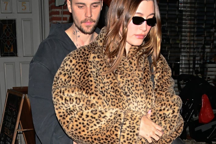 Justin Bieber in a cap hugs Hailey wearing an animal print coat and sunglasses, both walking outside