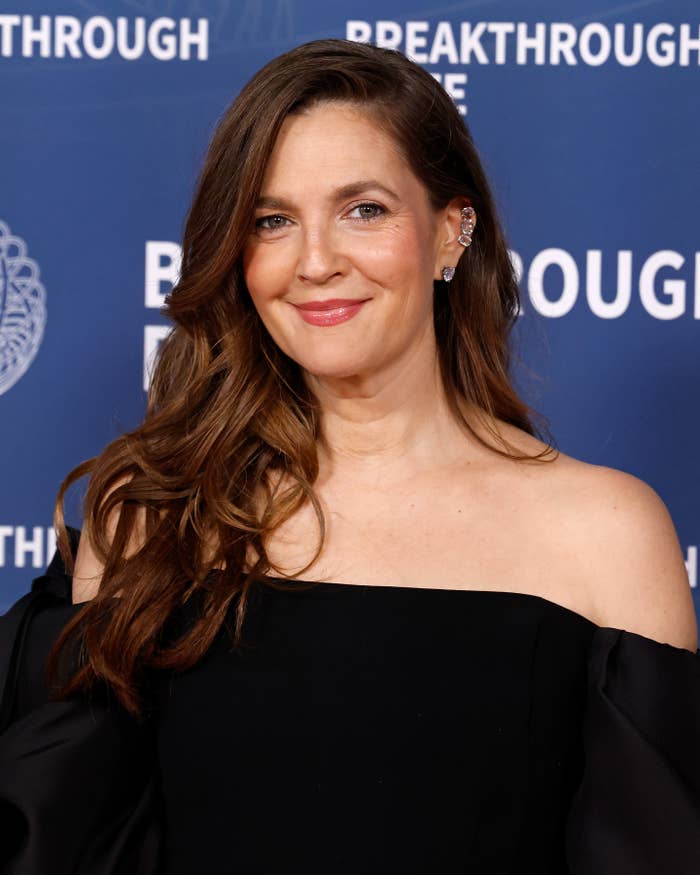 Person in an off-shoulder black dress at a formal event, smiling in front of a backdrop with 