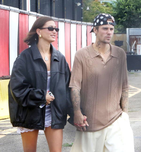 Hailey Bieber and Justin Bieber holding hands outside. Hailey wears a leather jacket, Justin a patterned cap and casual shirt