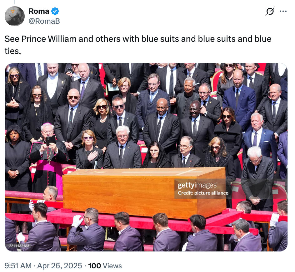 A group of people at a formal event surround a wooden casket. Many are wearing dark suits and ties