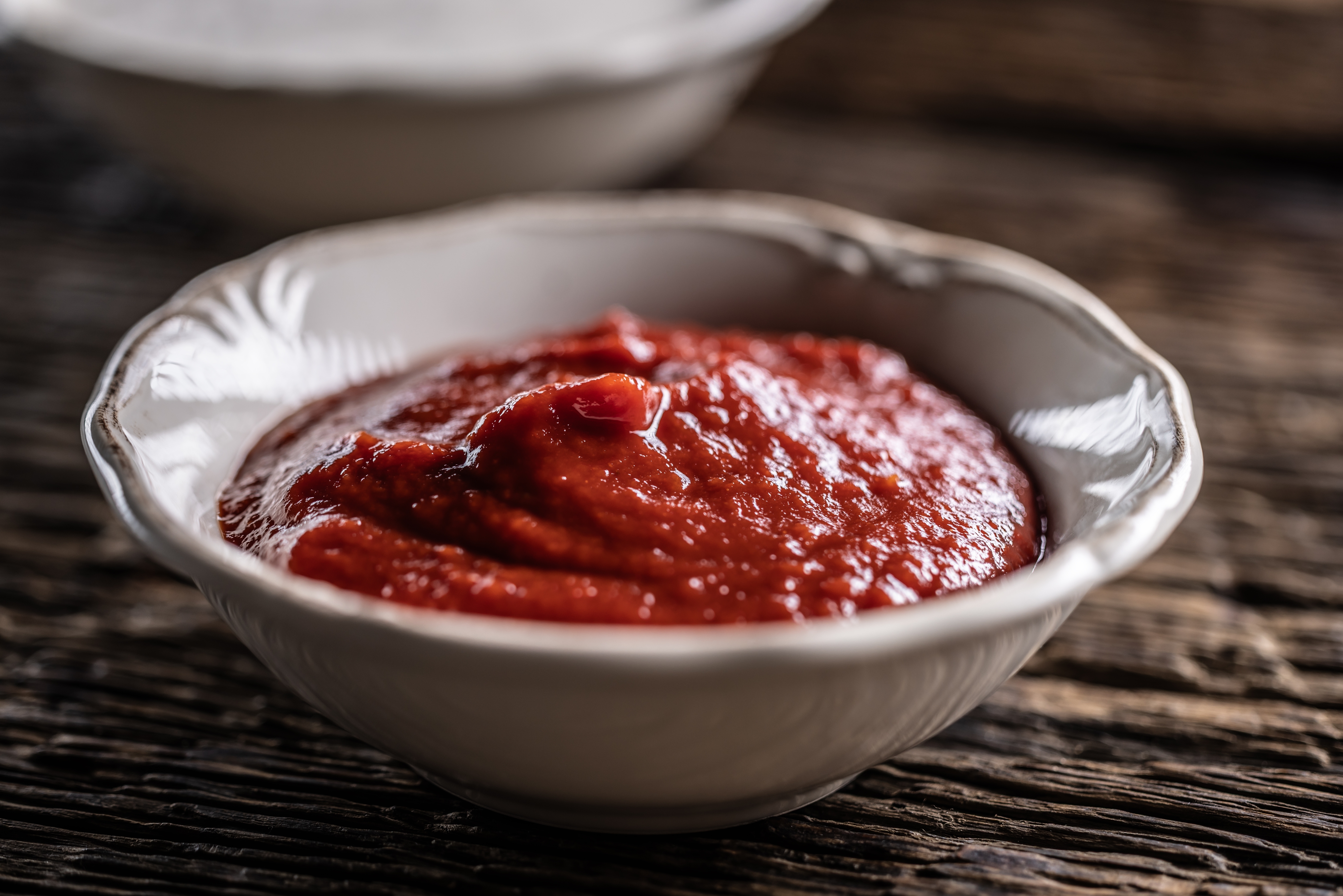 A bowl of thick red sauce sits on a rustic wooden surface