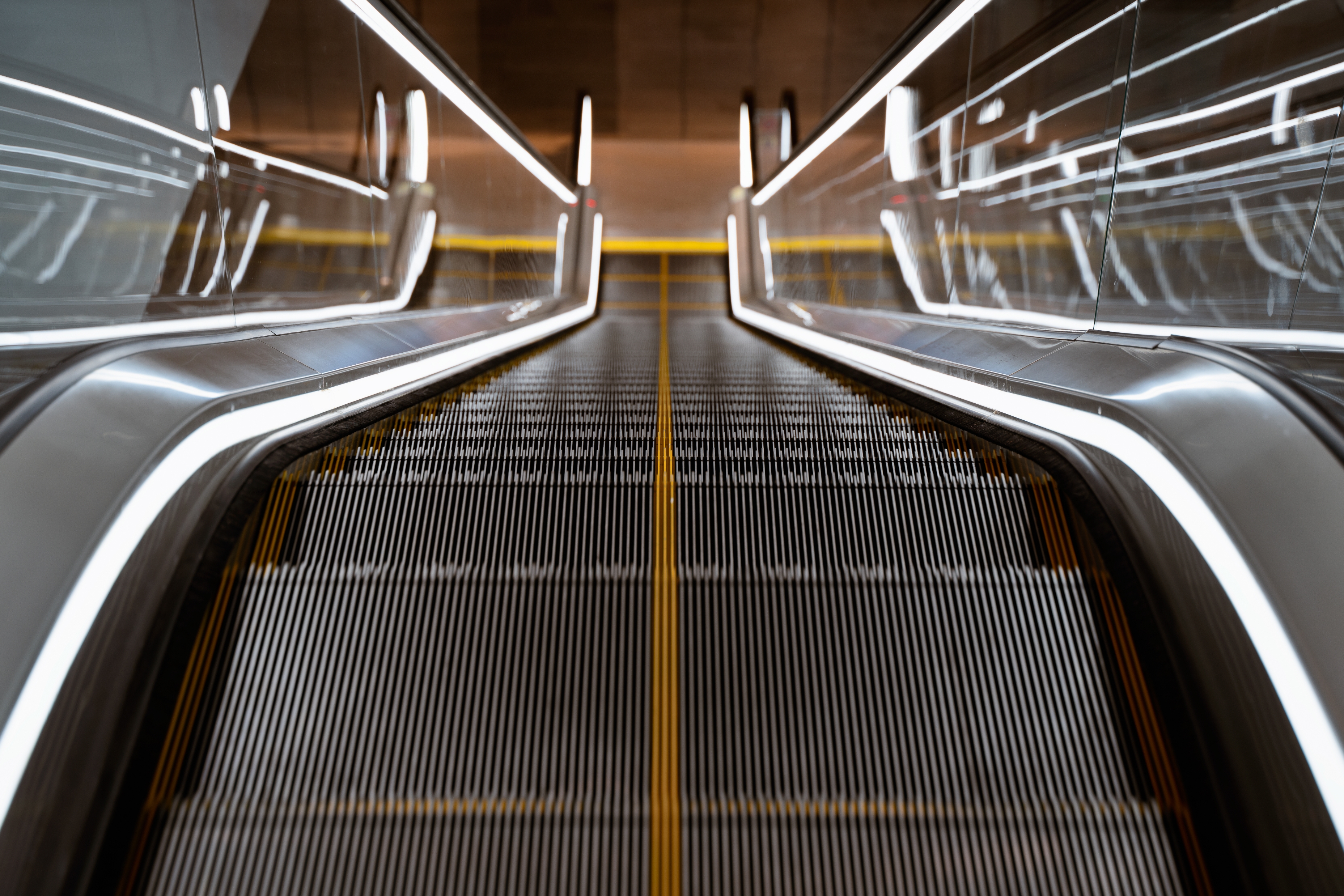 Escalator ascending between glass barriers, viewed from the bottom, leading upwards in a modern building