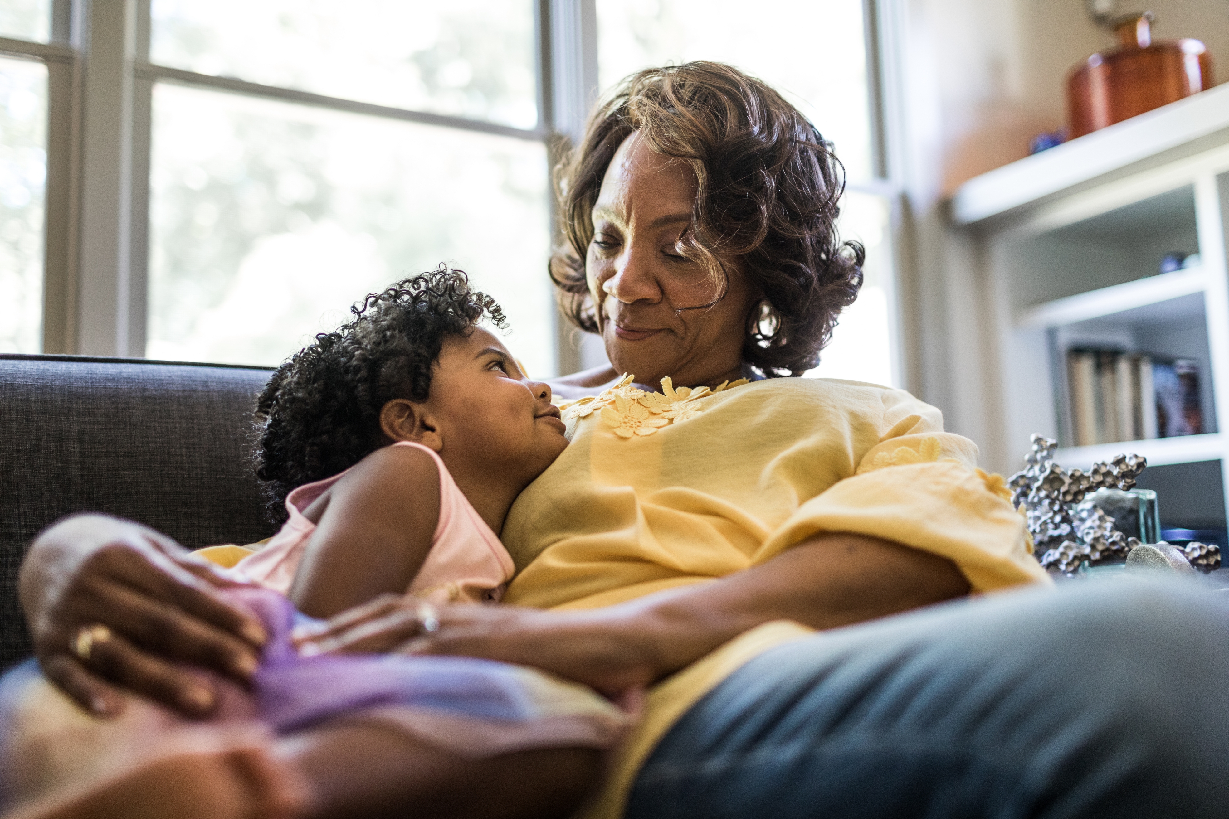 Woman lovingly holding a child on her lap in a living room, both smiling and making eye contact